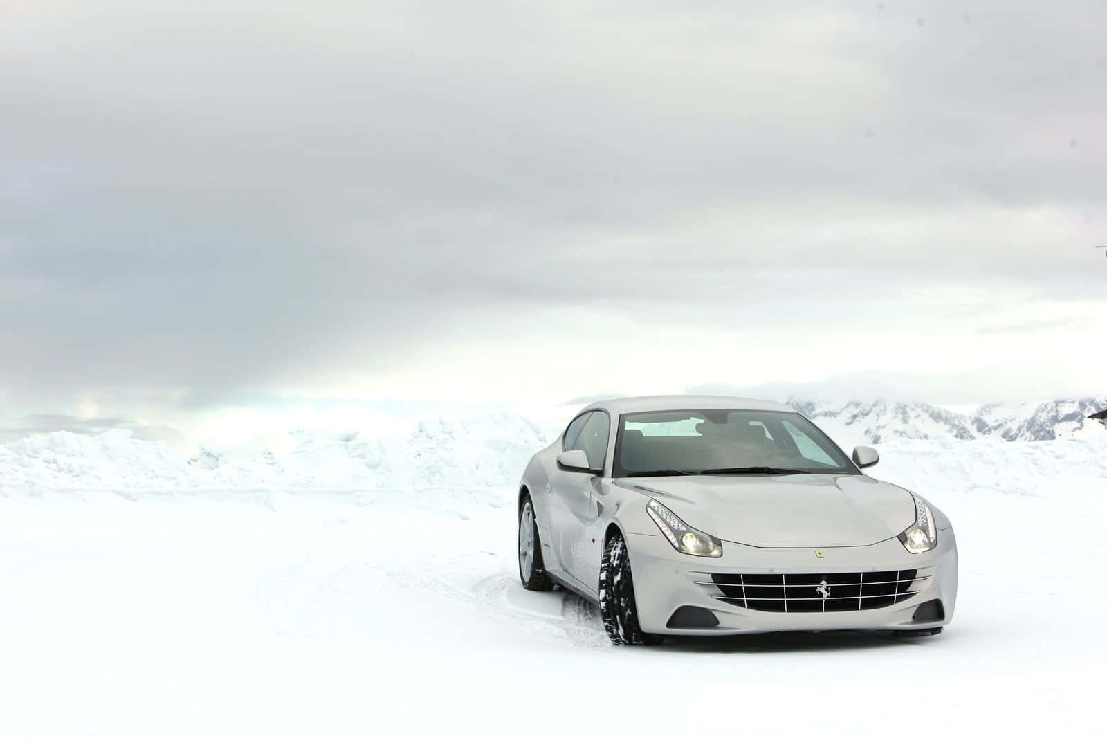 Ferrari Ff 桌布 壁紙 — 一輛時尚的銀色法拉利跑車在陰天下行駛在白雪覆蓋的山區景觀中。