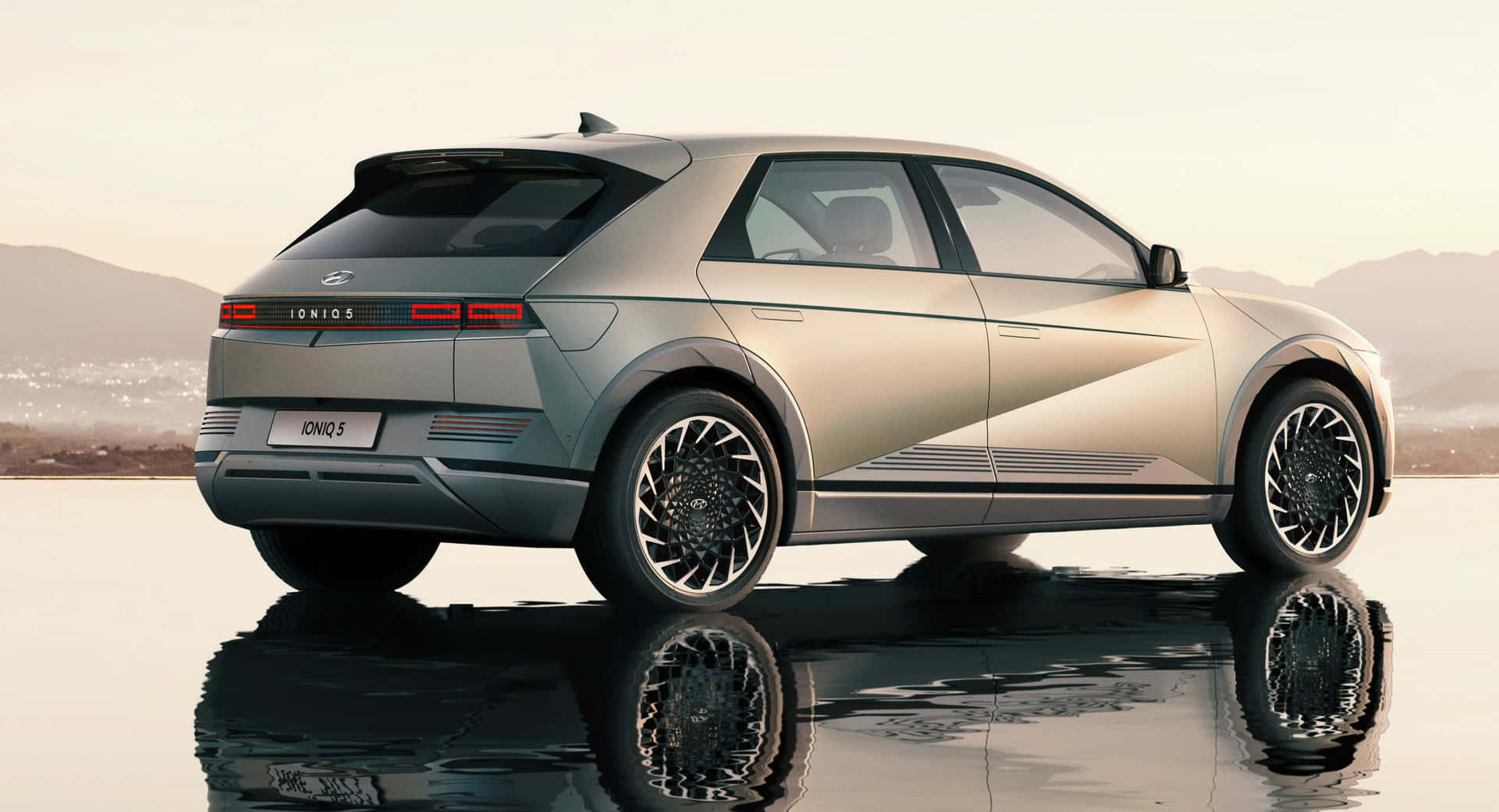 Hyundai 桌布 壁紙 — 一輛時尚的銀色現代IONIQ 5電動SUV在潮濕的路面上完美反射，背景是朦朧的山巒。