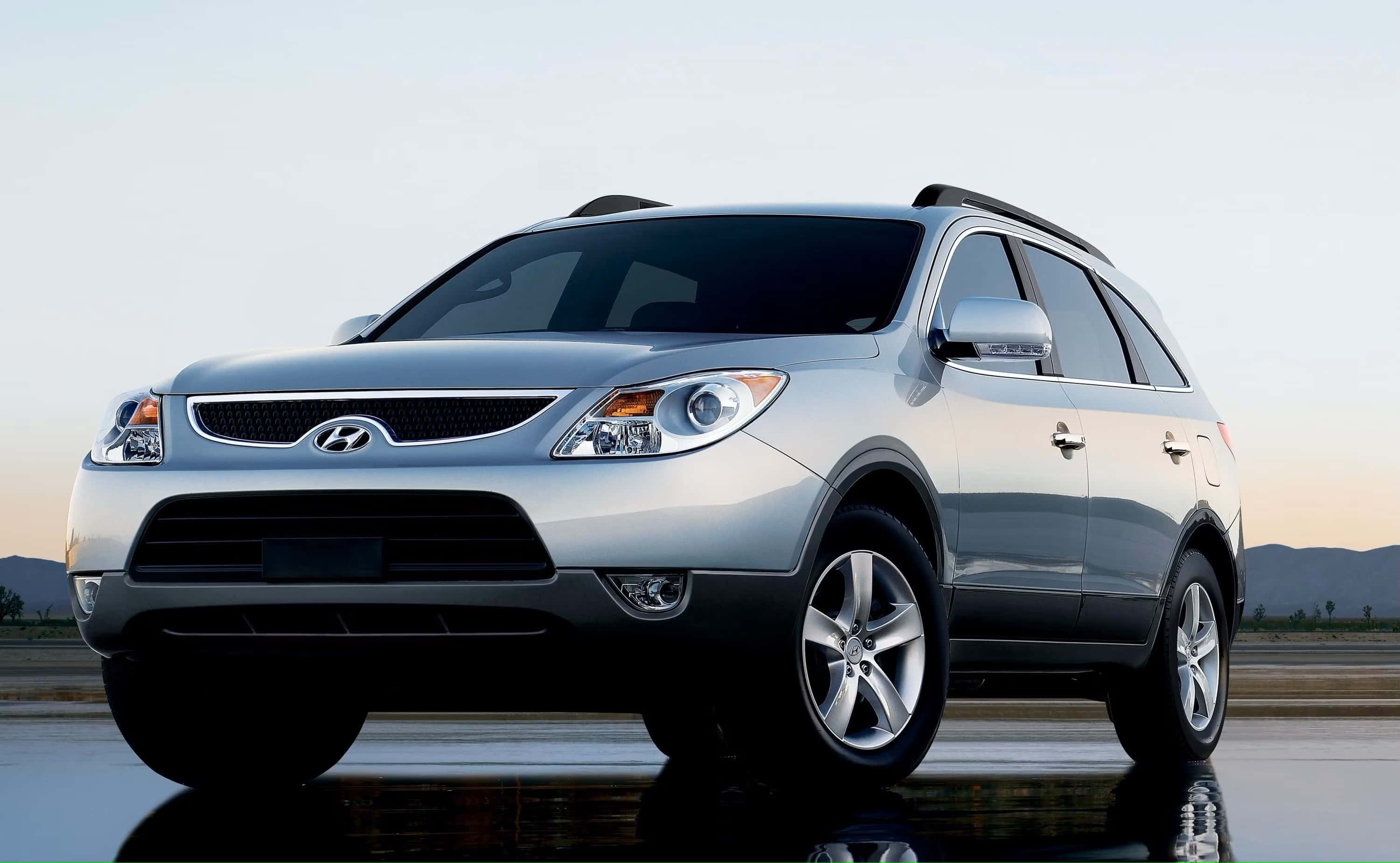 Hyundai Veracruz 桌布 壁紙 — 一輛時尚的銀色現代SUV停在潮濕的反光表面上，遠山在柔和的暮色天空下。