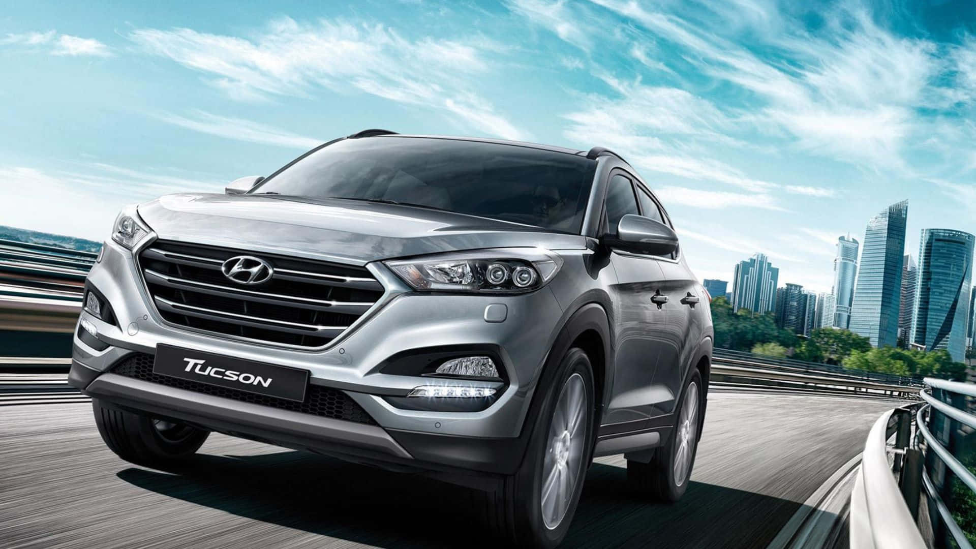 Hyundai Tucson 桌布 壁紙 — 一輛時尚的銀色現代Tucson SUV在高速公路上行駛，背景是現代化的城市天際線和藍天。