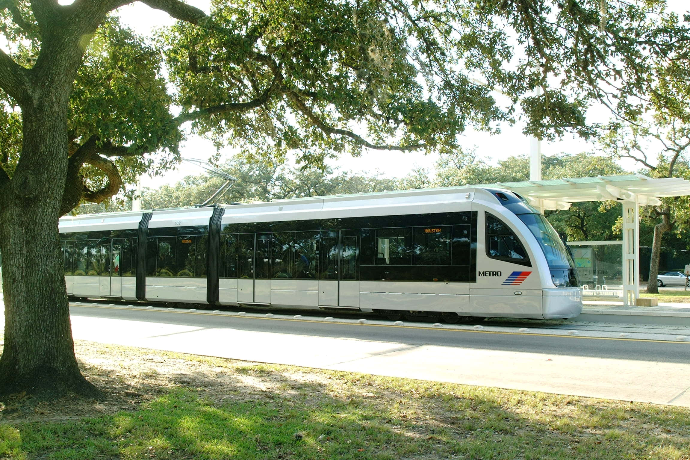 Metro 桌布 壁紙 — 一輛時尚的銀色現代電車在晴朗的日子裡，在茂密綠樹的樹冠下行駛。
