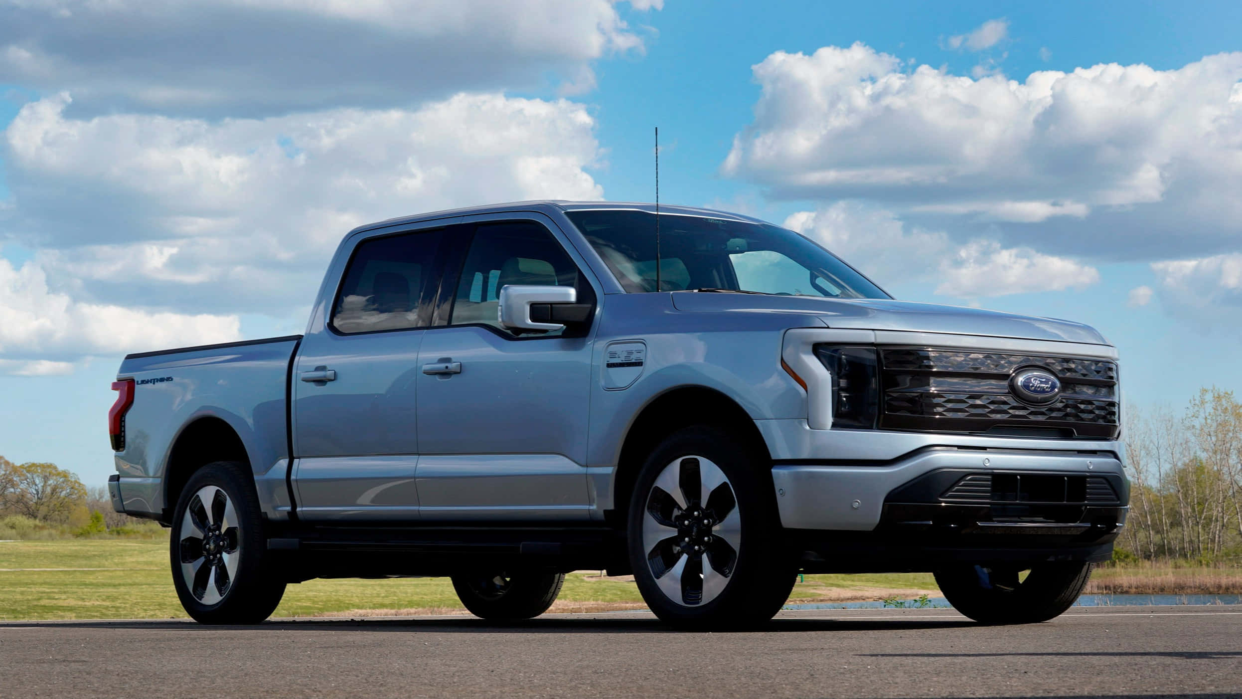 福特 桌布 壁紙 — 一輛時尚的銀色福特F-150 Lightning電動皮卡車停在瀝青路面上，頭頂是湛藍的天空和蓬鬆的白雲。