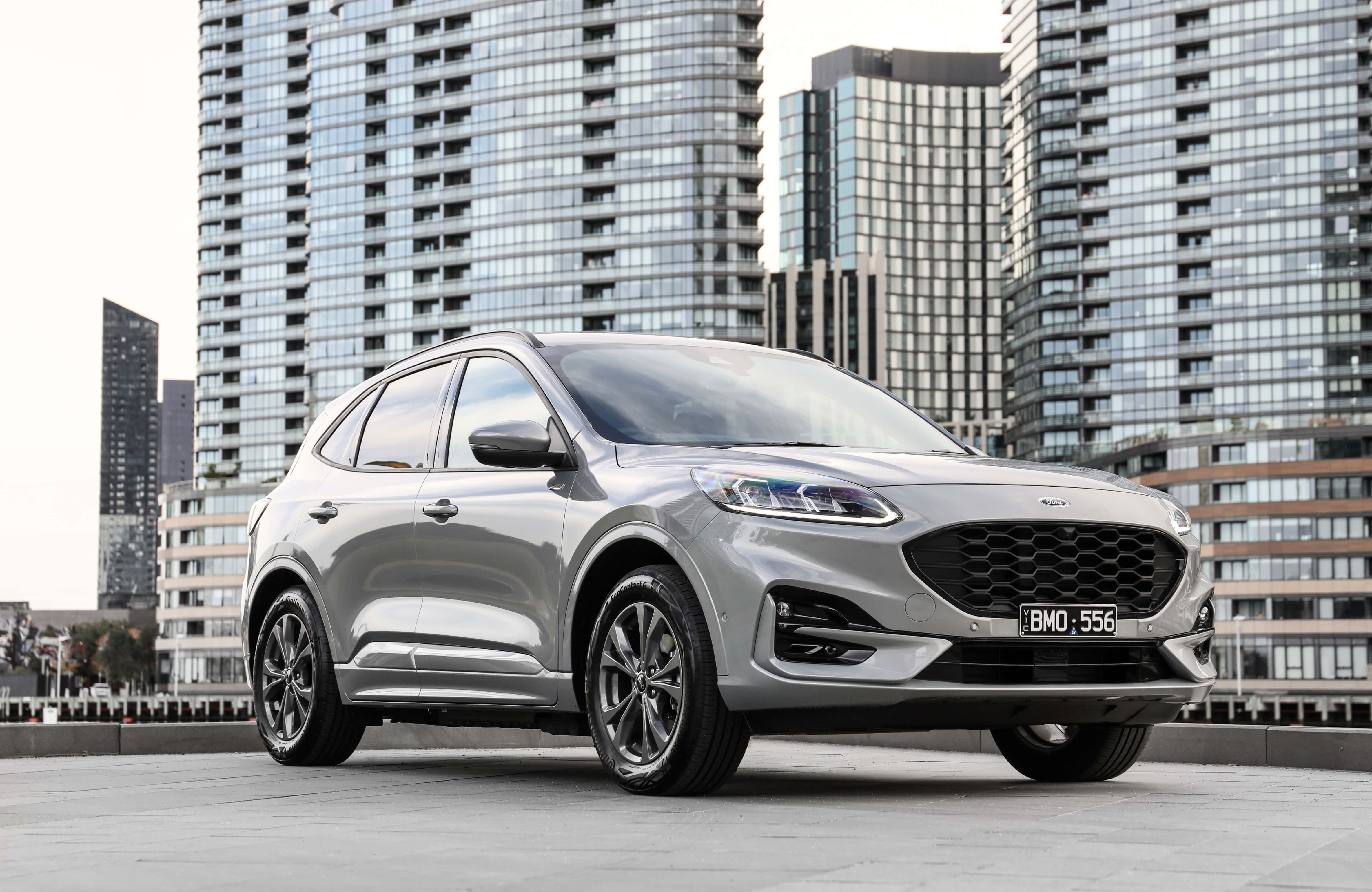 Ford Escape 桌布 壁紙 — 一輛時尚的銀色福特Kuga SUV停放在屋頂上，背後有現代玻璃摩天大樓聳立。