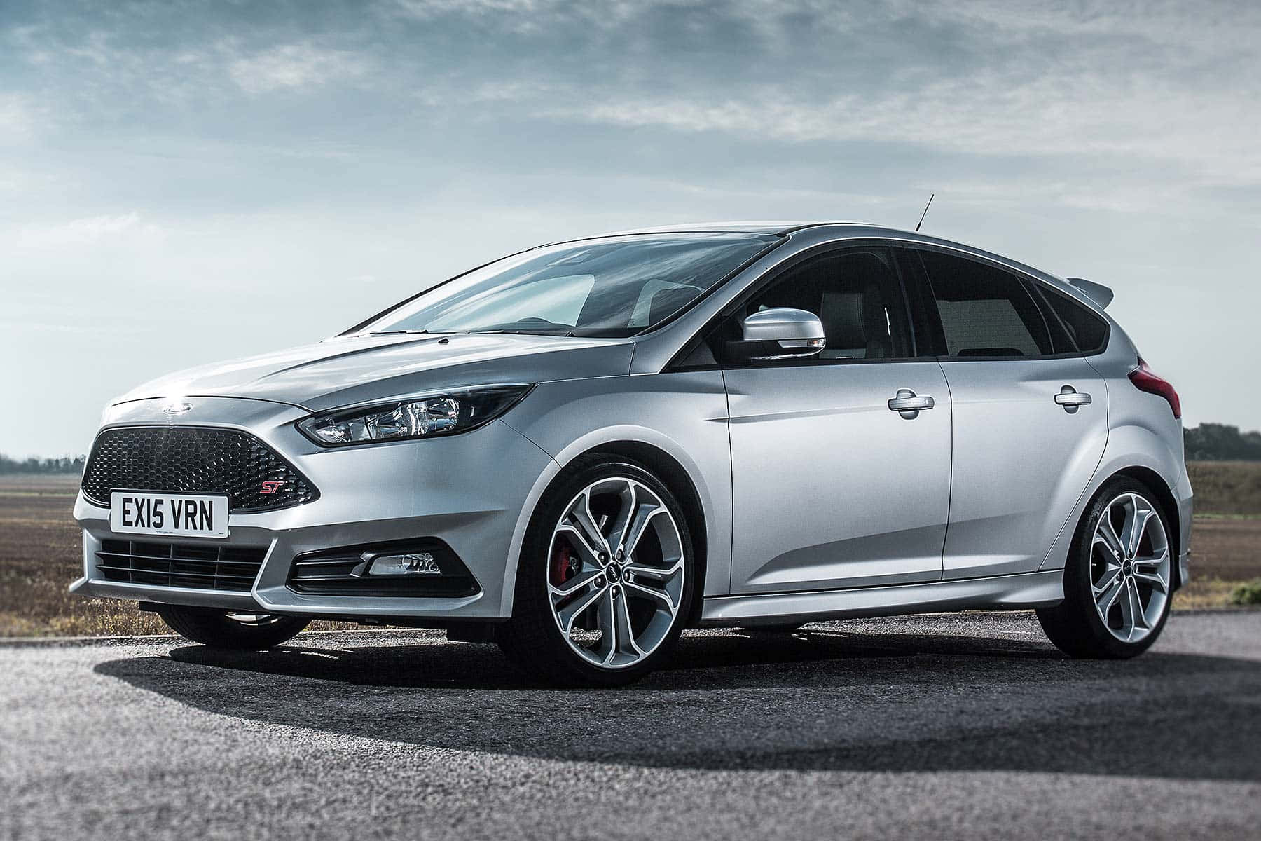 Ford Focus 桌布 壁紙 — 一輛時尚的銀色福特福克斯ST停泊在瀝青路上，天空多雲，遠處有田野。