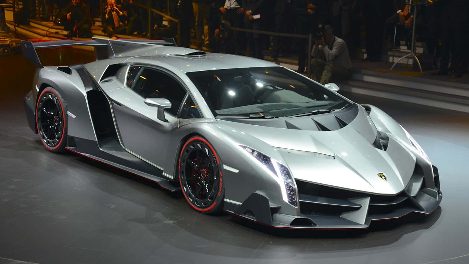 Lamborghini Veneno 桌布 壁紙 — 一輛時尚的銀色藍寶堅尼 Veneno，配以紅色點綴的車輪，在車展的明亮燈光下閃閃發光。