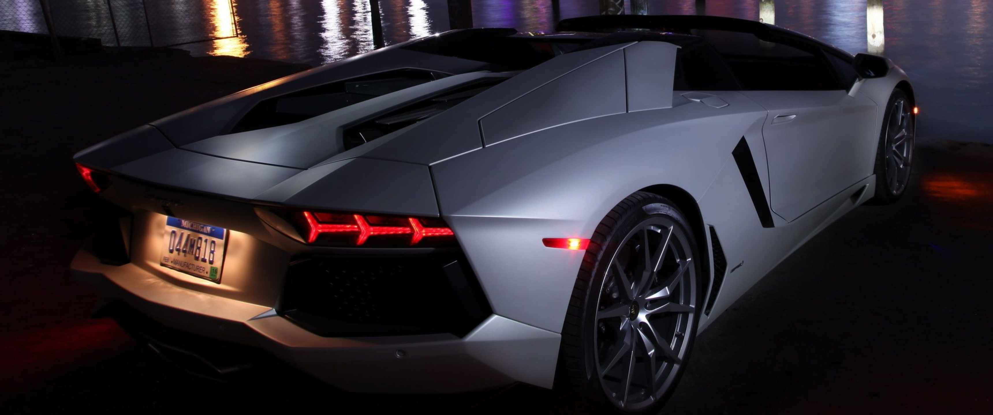 3440x1440p Lamborghini 桌布 壁紙 — 一輛時尚的銀色藍寶堅尼Aventador跑車在夜間霓虹燈下閃耀，在濕漉漉的路面上留下倒影。