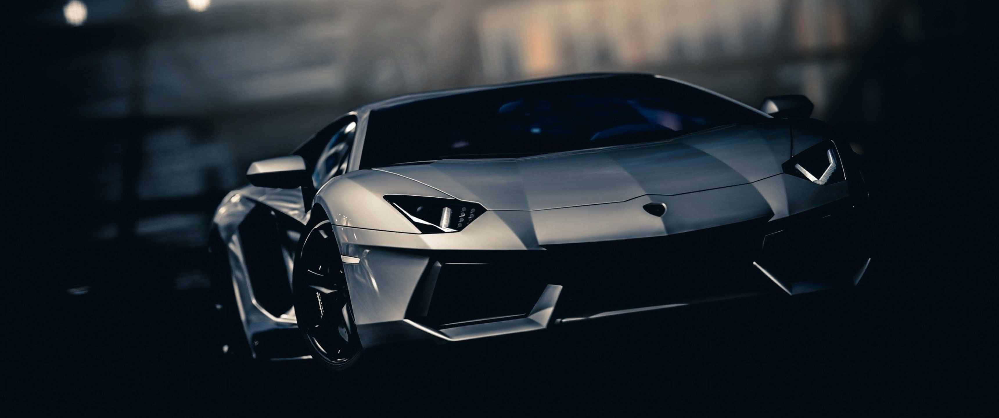 3440x1440p Lamborghini 桌布 壁紙 — 一輛時尚的銀色藍寶堅尼Aventador在昏暗的城市燈光下閃耀，具有銳利的棱角線條和發光的車頭燈。