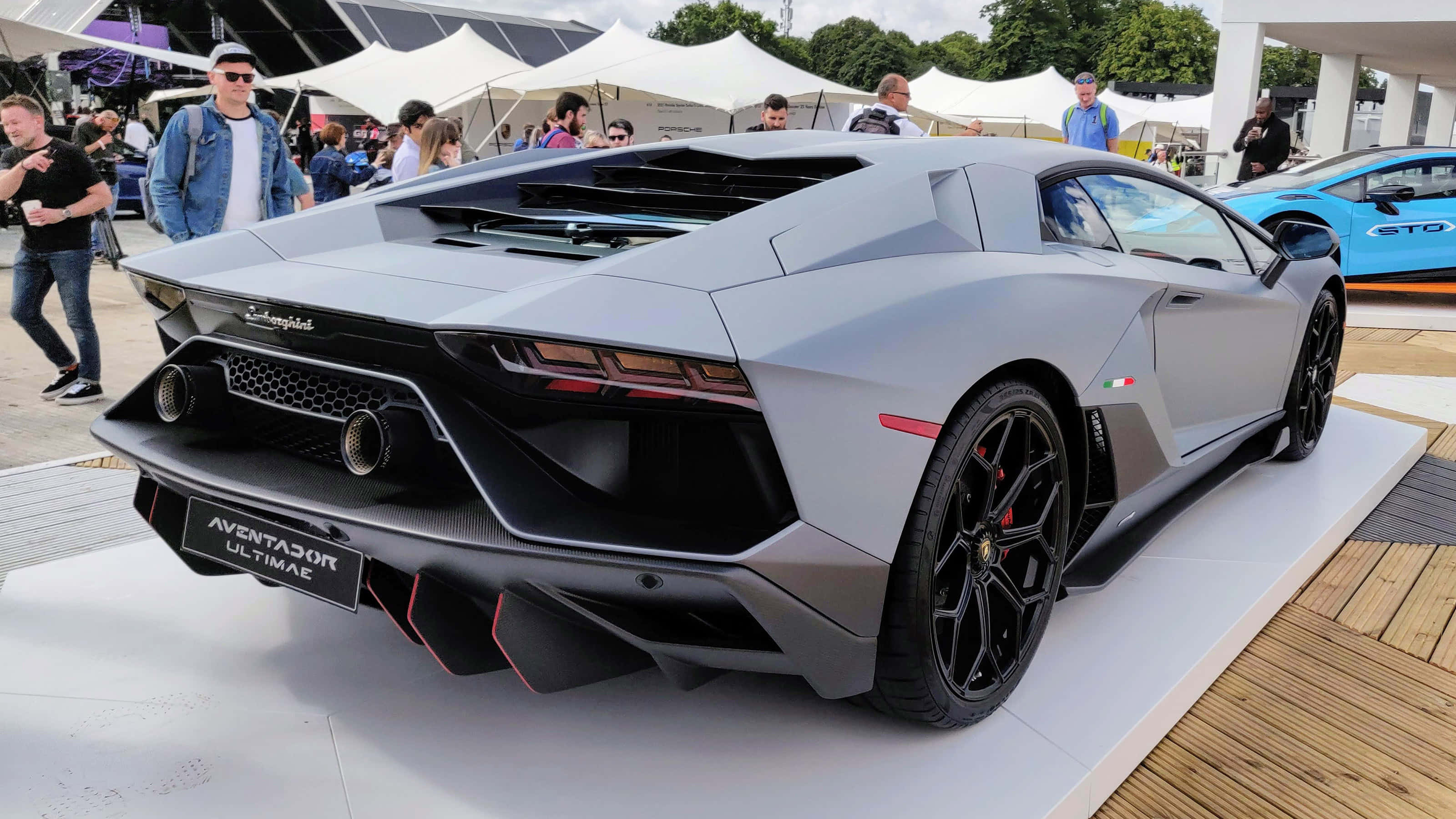 Car Side View 桌布 壁紙 — 一輛時尚的銀色藍寶堅尼Aventador Ultimae在戶外車展上展出，背景有人群和白色帳篷。