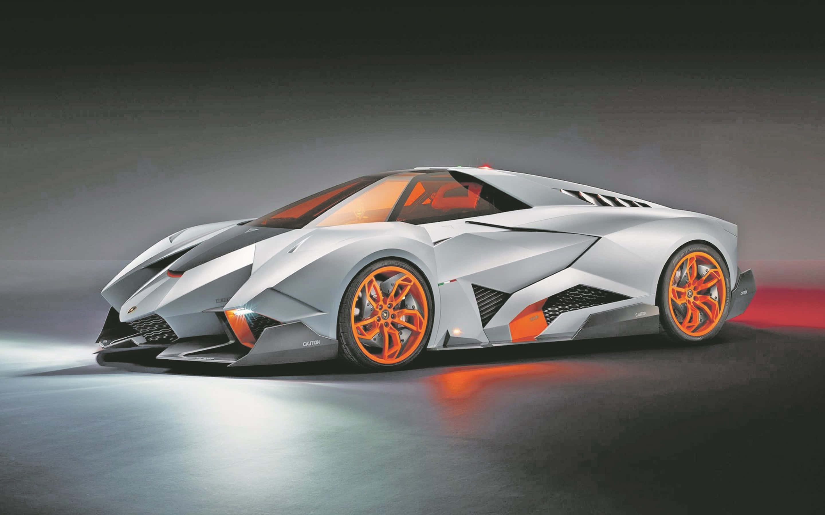 Cool Lamborghinis 桌布 壁紙 — 一輛時尚的銀色藍寶堅尼概念車，帶有充滿活力的橙色車輪和裝飾，在暗色地板上的工作室燈光下閃耀。