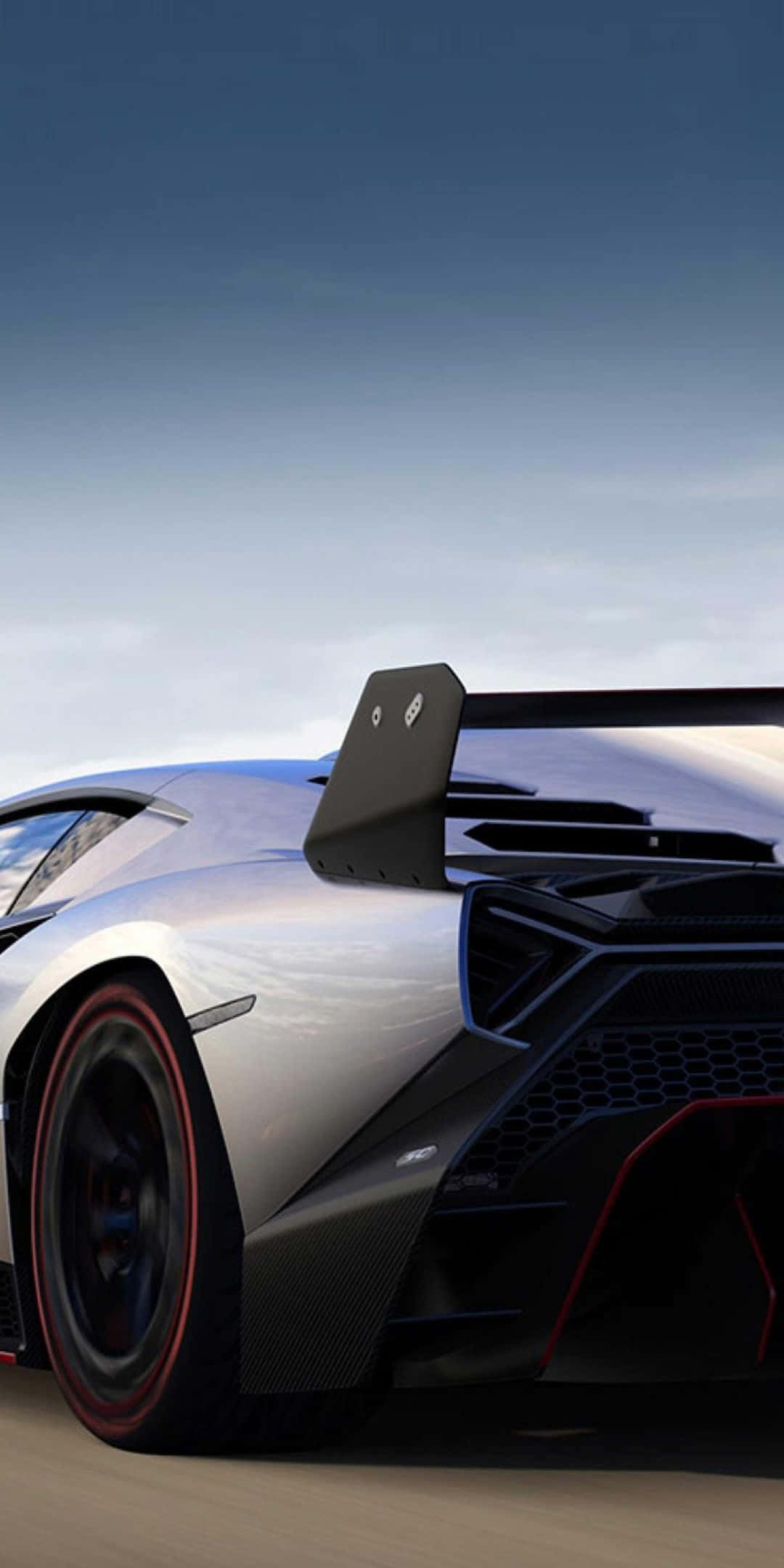 Pixel 3 Lamborghini 桌布 壁紙 — 一輛時尚的銀色藍寶堅尼跑車，帶有黑色碳纖維飾邊和紅色點綴，在晴朗的藍天下沿著沙漠公路飛馳。