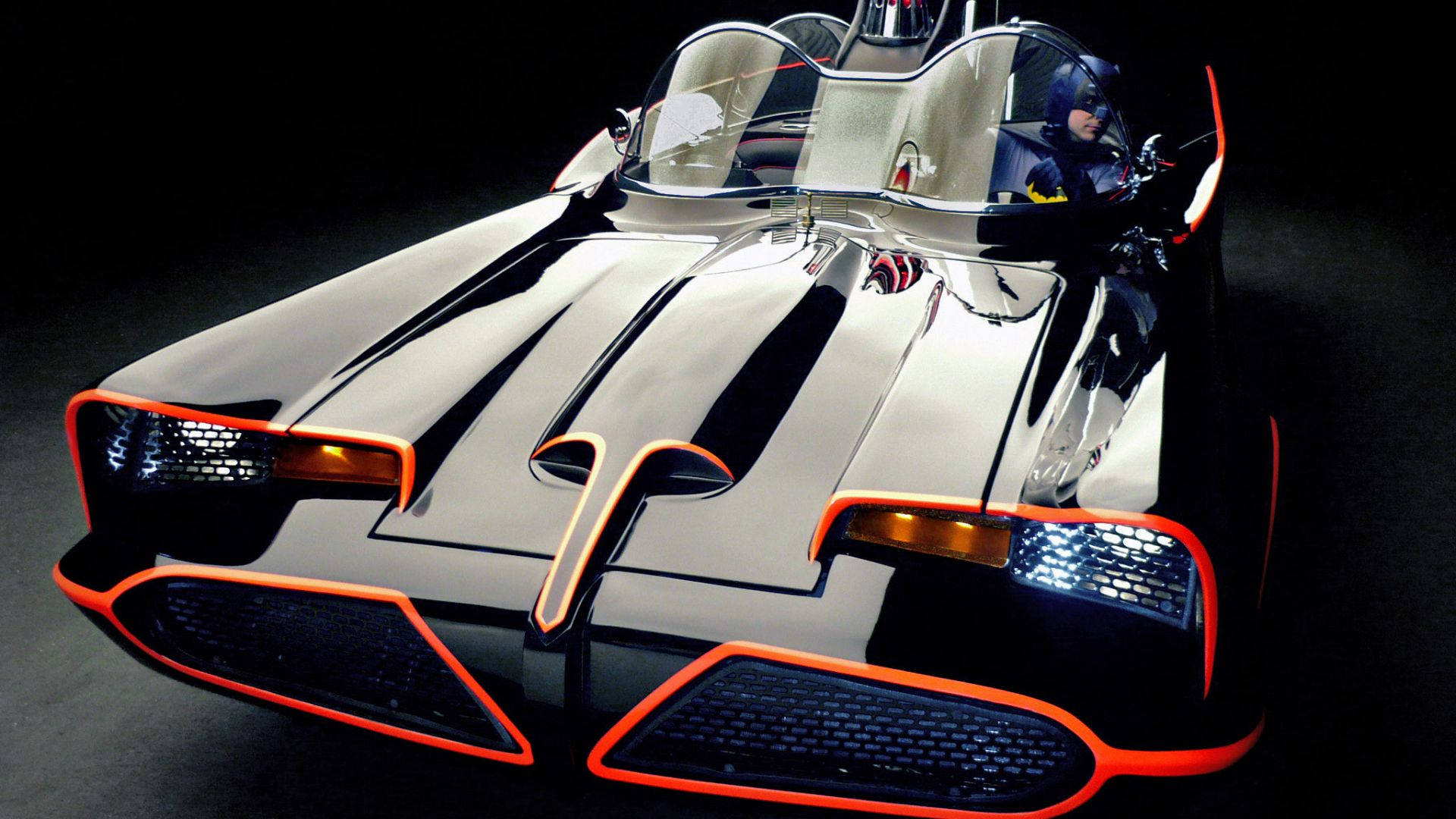 Batmobile 桌布 壁紙 — 一輛時尚的銀色蝙蝠車，帶有發光的橙色飾邊，駕駛者戴著頭罩，在戲劇性的工作室燈光下拍攝。