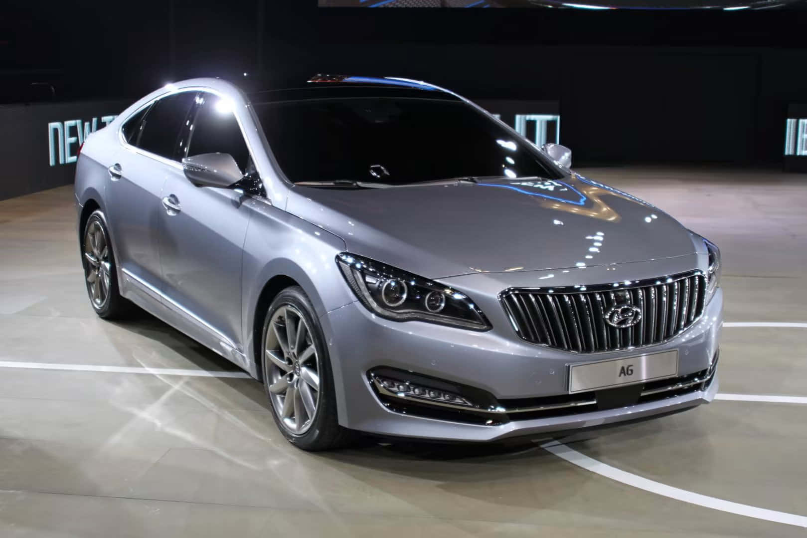 Hyundai 桌布 壁紙 — 一輛時尚的銀色豪華轎車在明亮的展廳燈光下，在帶有白色標記的拋光地板上閃閃發光。