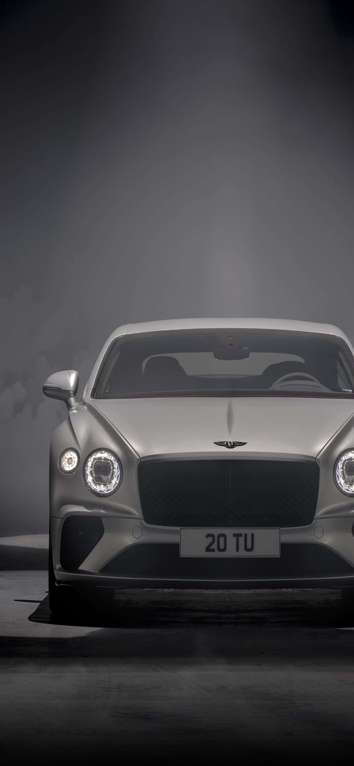 iPhone Xs Max Bentley 桌布 壁紙 — 一輛時尚的銀色賓利 Bentayga 在煙霧瀰漫的深色工作室背景下被聚光燈照亮。
