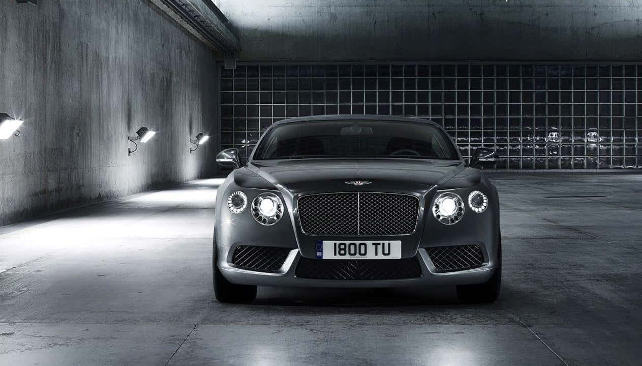 bentley HD 桌布 壁紙 — 一輛時尚的銀色賓利 Continental GT 在極簡混凝土車庫的聚光燈下閃閃發光，車庫牆壁帶有網格圖案。