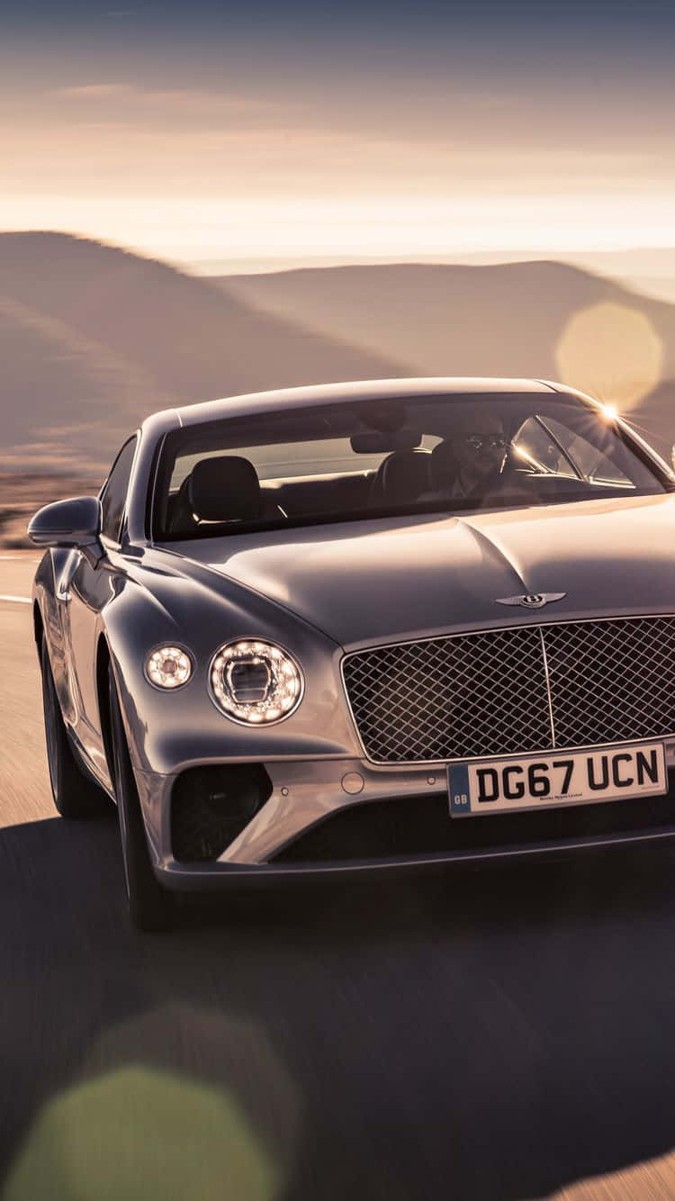bentley HD 桌布 壁紙 — 一輛時尚的銀色賓利 Continental GT 在日落時分沿著沙漠公路疾馳，背景是起伏的山丘。