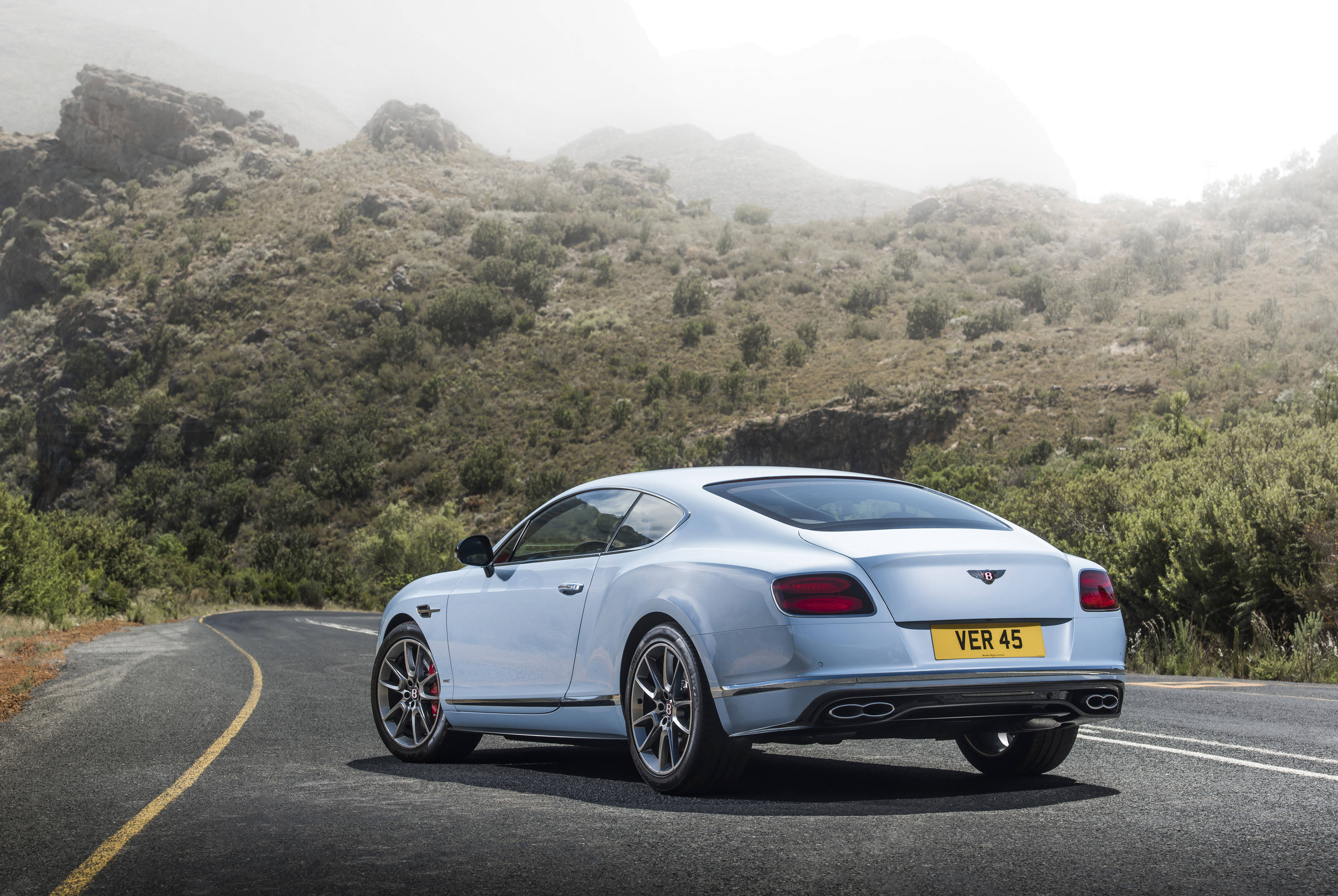 bentley HD 桌布 壁紙 — 一輛時尚的銀色賓利 Continental GT 沿著蜿蜒的山路行駛，穿過霧氣瀰漫的綠色山丘。