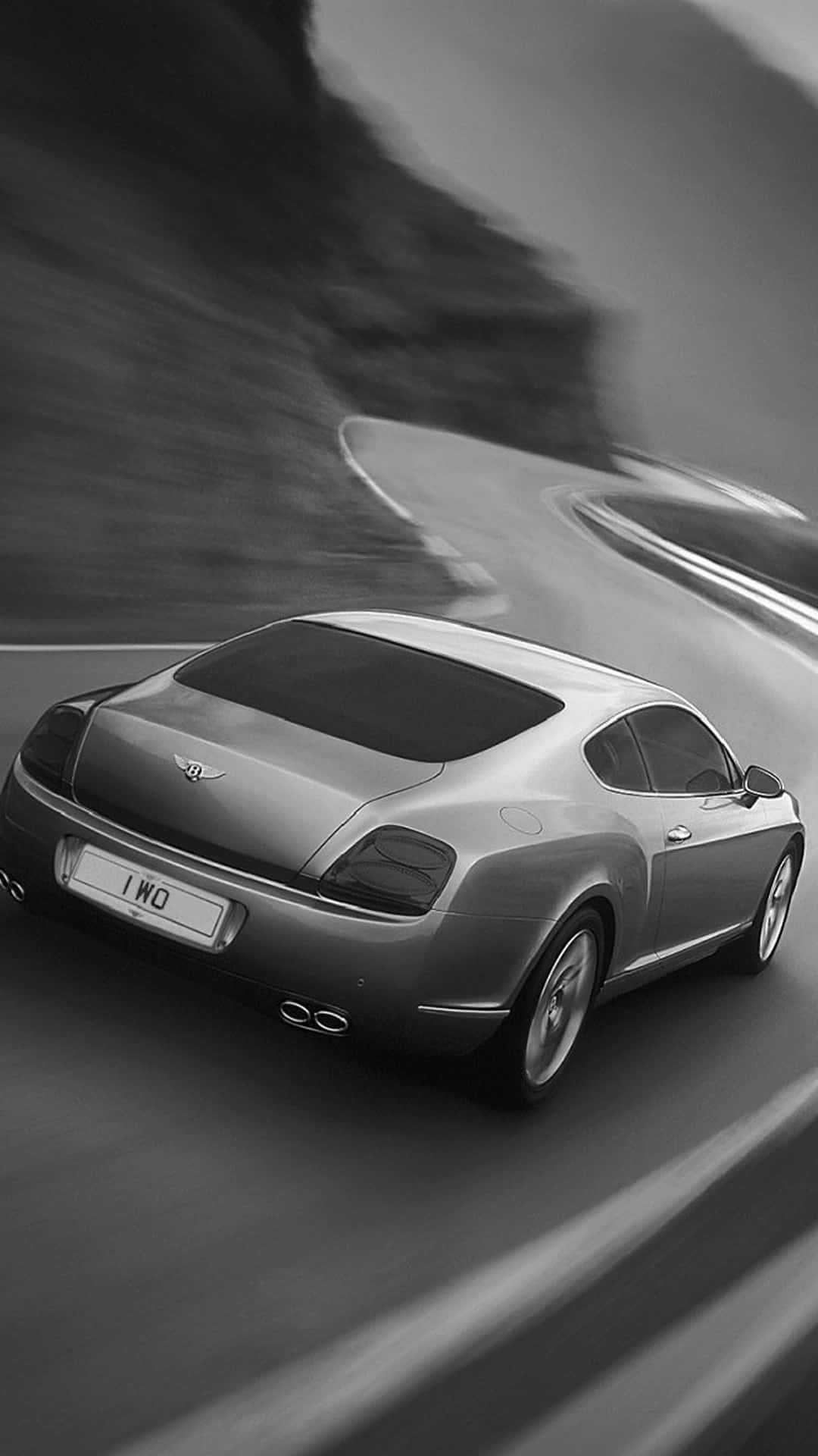 汽車 iPhone 壁紙 桌布 壁紙 — 一輛時尚的銀色賓利 Continental GT 在戲劇性的黑白動態模糊中沿著蜿蜒的山路疾馳。