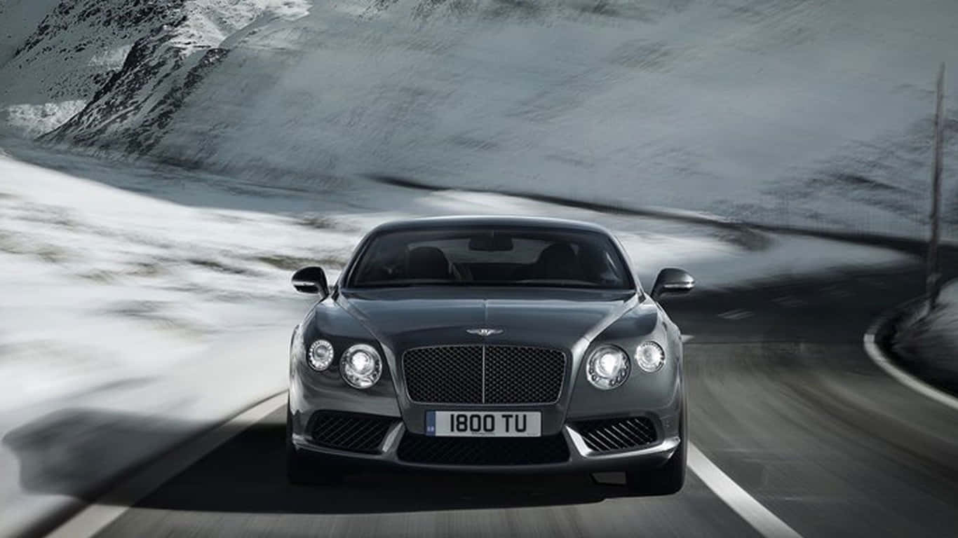 1366x768 Bentley 桌布 壁紙 — 一輛時尚的銀色賓利 Continental GT 在蜿蜒的積雪山路上疾馳，帶有模糊的動感。