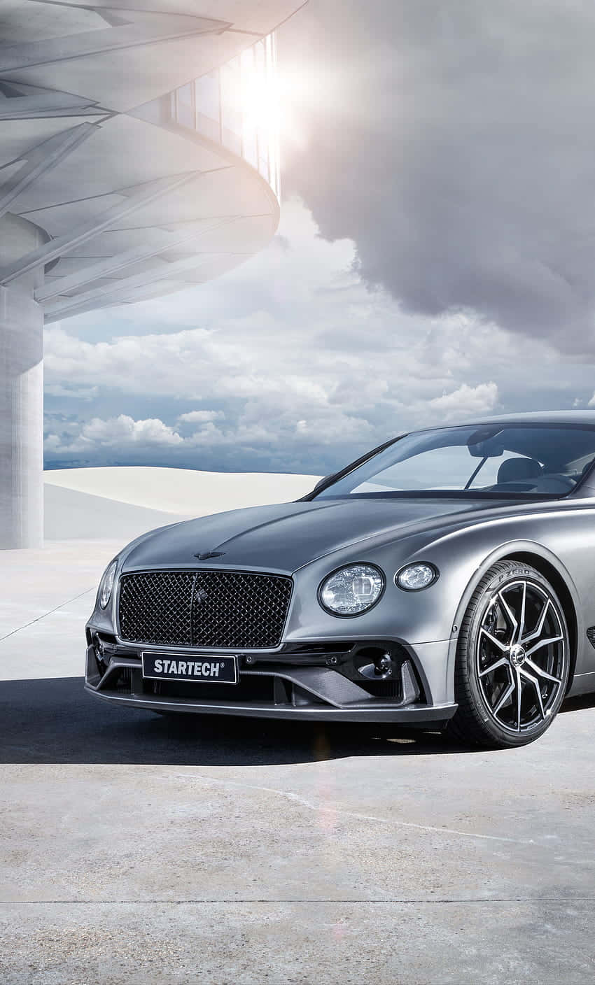 Bentley Continental Gt 桌布 壁紙 — 一輛時尚的銀色賓利，配備Startech改裝，停放在現代混凝土結構下，背景是陰天。