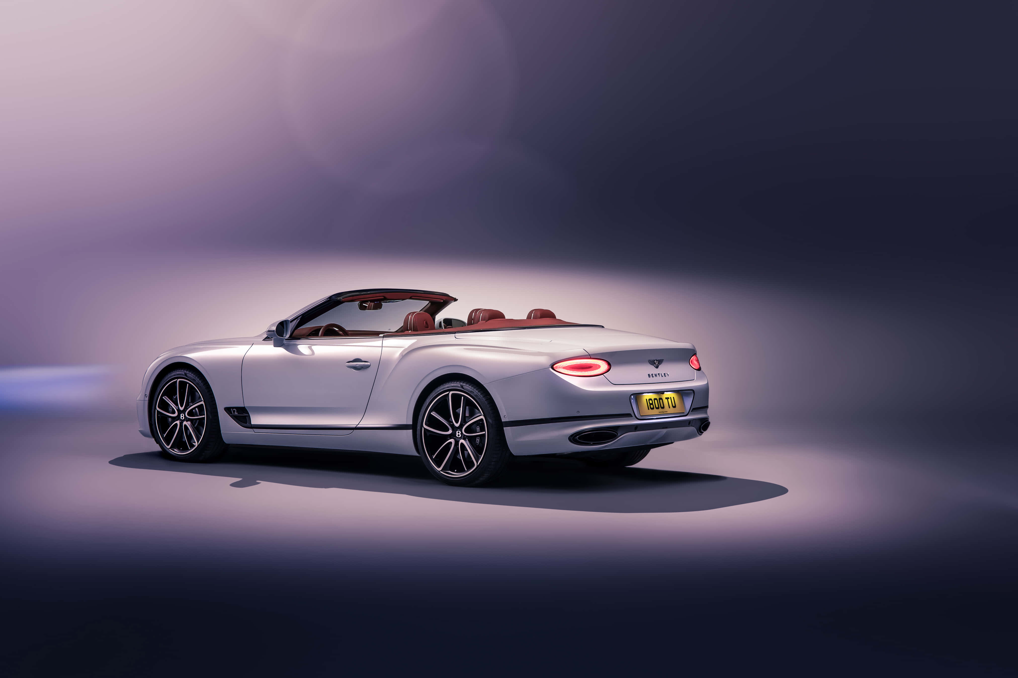 Bentley Continental Gt Convertible 桌布 壁紙 — 一輛時尚的銀色賓利敞篷車，配紅色皮革座椅，在柔和的紫色工作室燈光下閃耀。