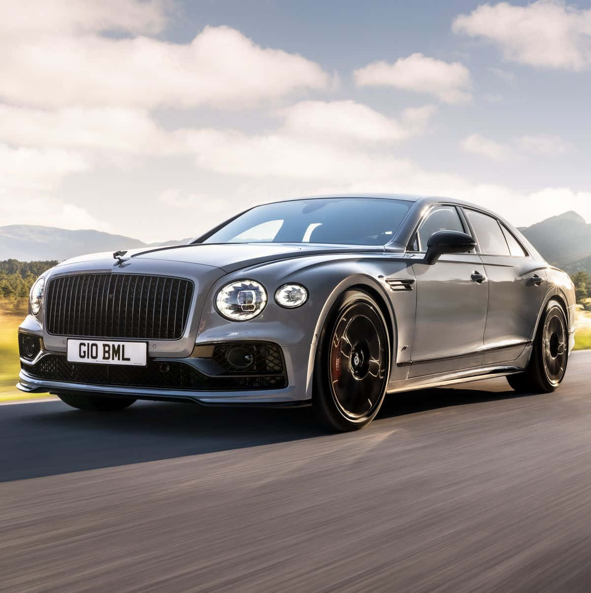 Bentley Flying Spur 桌布 壁紙 — 一輛時尚的銀色賓利飛馳在部分多雲的天空下沿著山路疾馳。