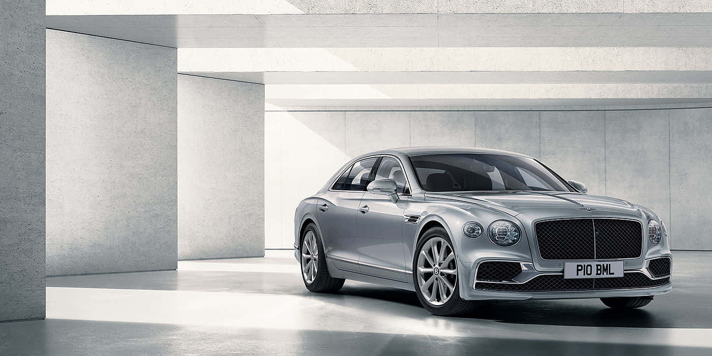 Bentley Flying Spur 桌布 壁紙 — 一輛時尚的銀色賓利飛馳轎車在簡約的混凝土車庫中閃耀著明亮的光芒。