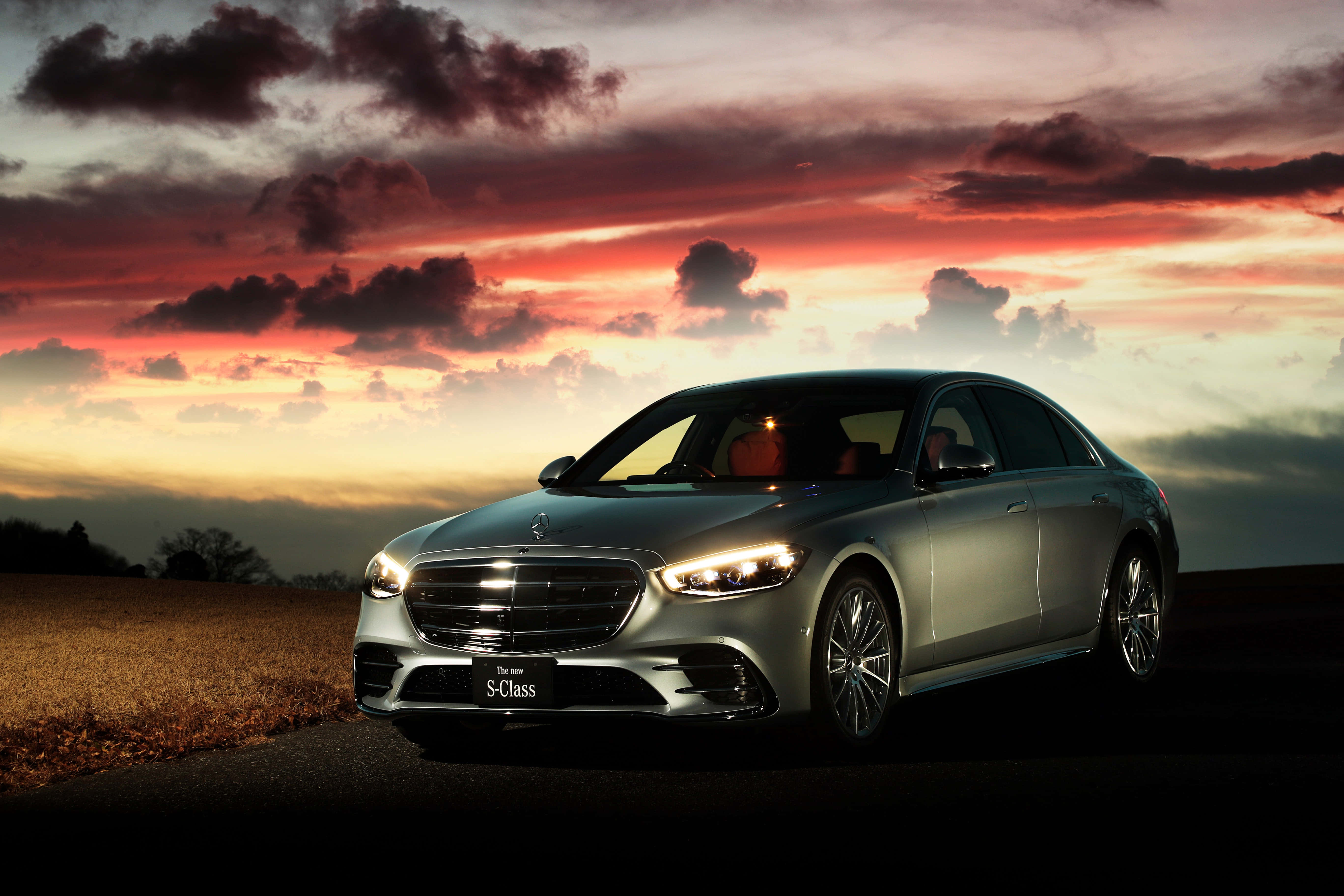 Mercedes Car 4K 桌布 壁紙 — 一輛時尚的銀色賓士S-Class轎車在戲劇性的雲彩下，於熾熱的日落天空中閃耀。