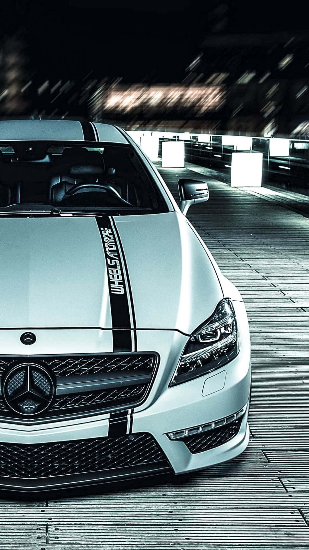 Mercedes 桌布 壁紙 — 一輛時尚的銀色賓士跑車帶有黑色賽車條紋，停放在木製平台上，在戲劇性的夜間燈光下。