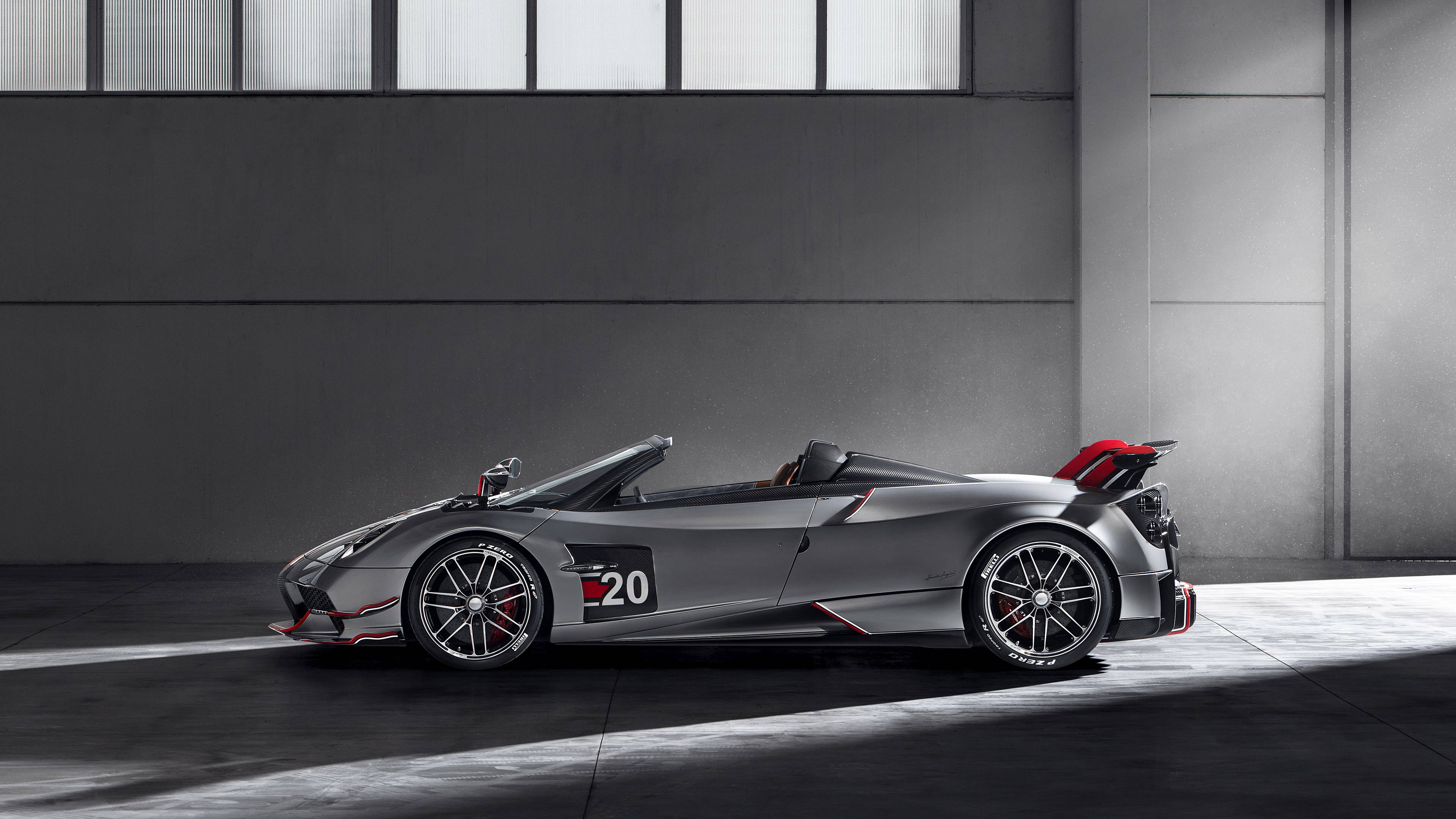 pagani iPhone 桌布 壁紙 — 一輛時尚的銀色賽車，帶有紅色點綴和20號，停在明亮光線下的簡約工業車庫中。