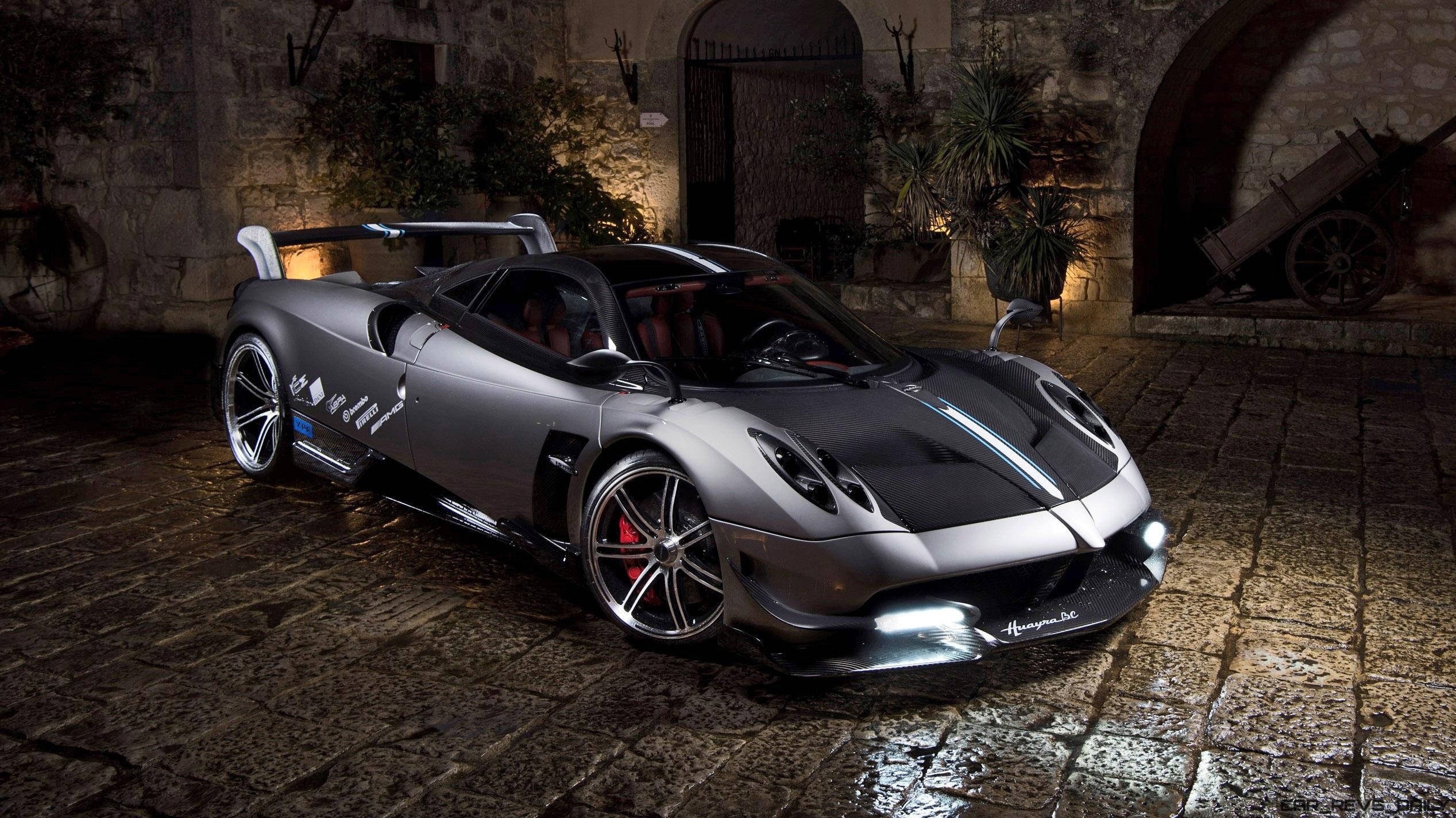 Pagani 桌布 壁紙 — 一輛時尚的銀色超級跑車，車頭燈閃爍，夜晚停在濕漉漉的鵝卵石庭院中，上方是溫暖的石拱門。