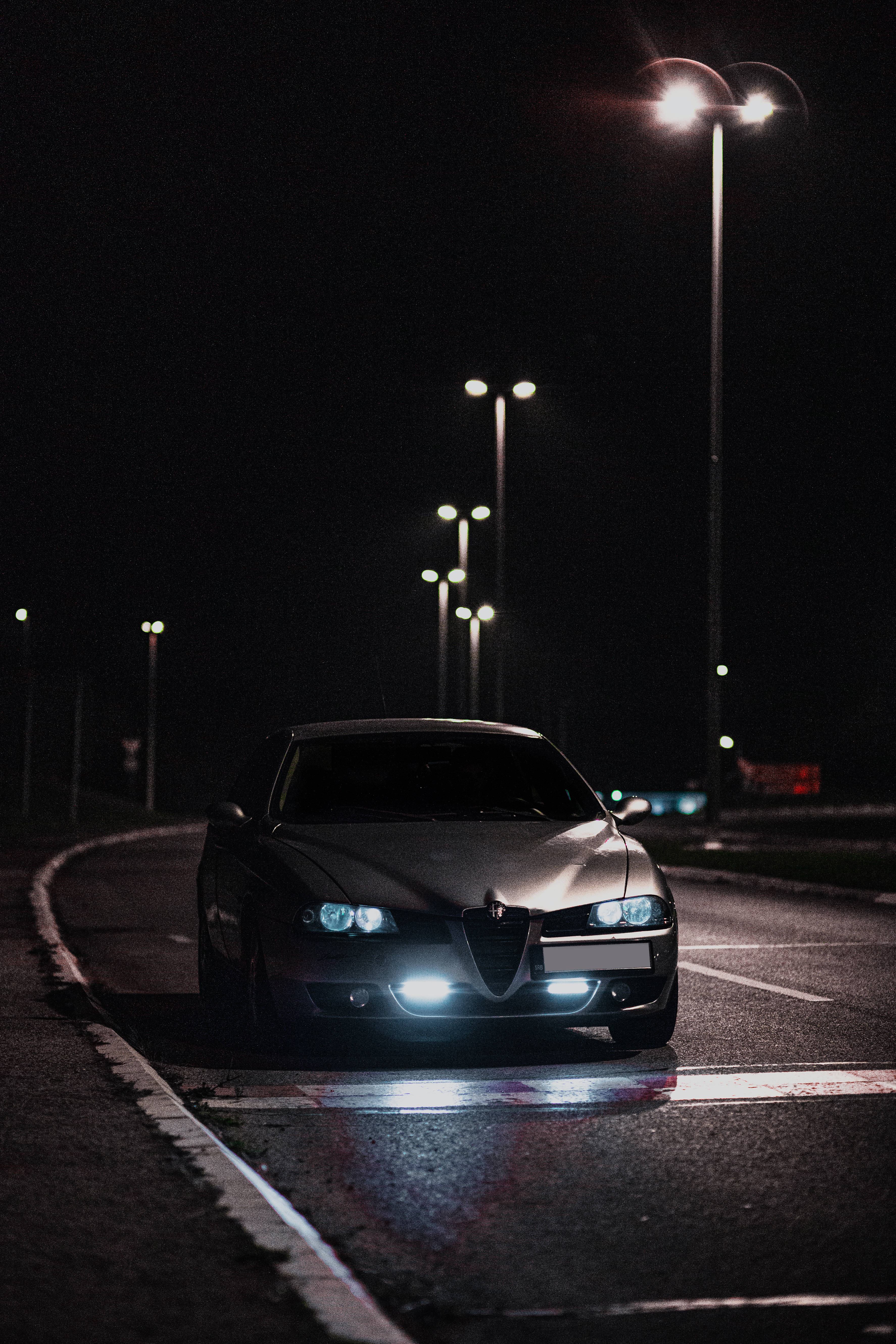 Alfa Romeo 桌布 壁紙 — 一輛時尚的銀色跑車，車頭燈閃爍，夜間停在潮濕的道路上，明亮的街燈下。