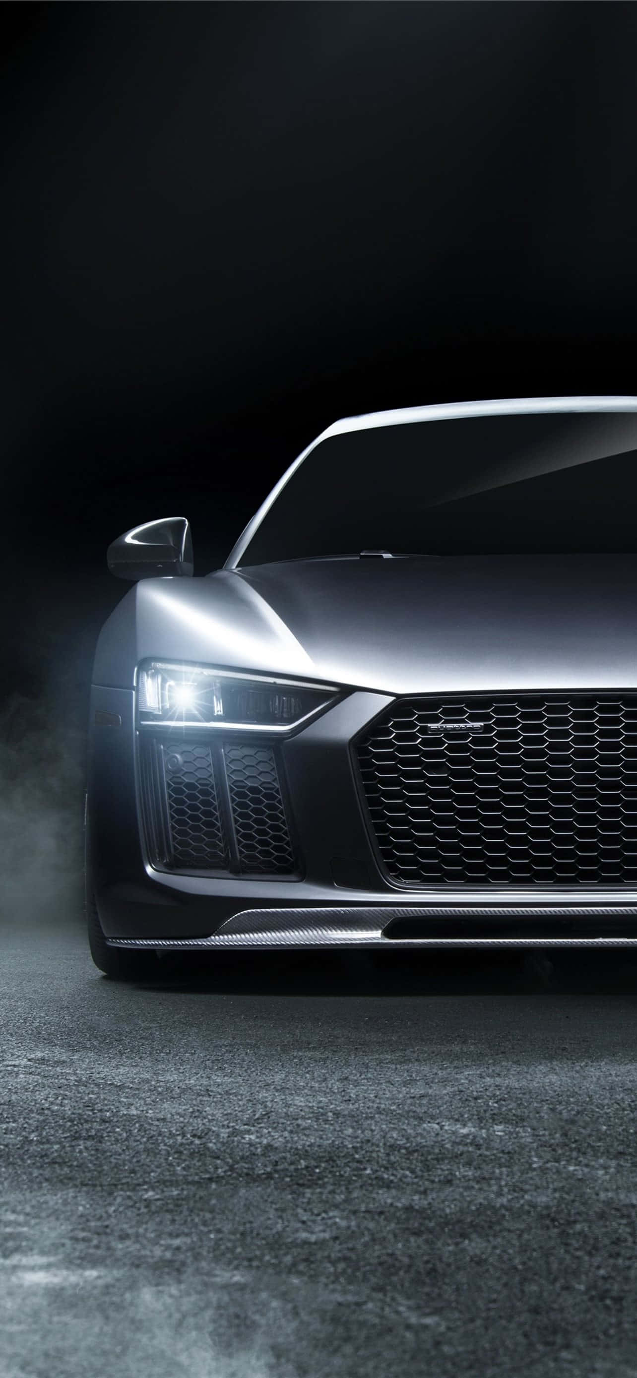 Audi iPhone 桌布 壁紙 — 一輛時尚的銀色跑車，配備發光的頭燈和碳纖維飾件，在戲劇性的工作室燈光下，停在黑暗潮濕的路面上。