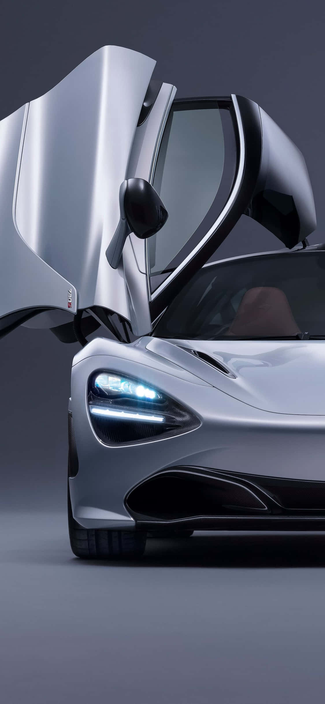 iPhone Xs Mclaren 720s 桌布 壁紙 — 一輛時尚的銀色跑車，鷗翼門在深色工作室背景下打開。