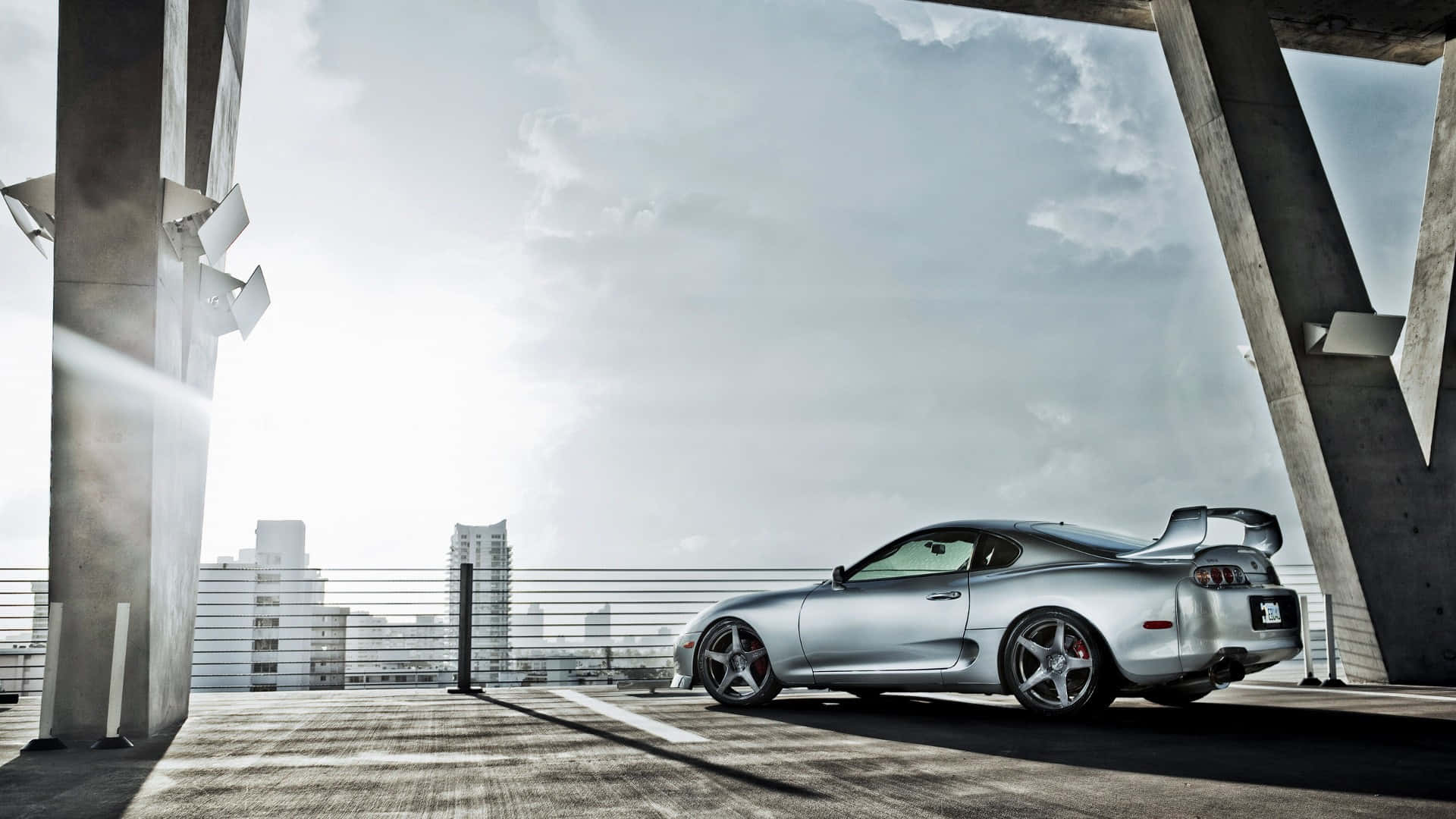 銀色跑車停放在屋頂上，背景為城市天際線。 — Toyota Supra Mk4 壁紙