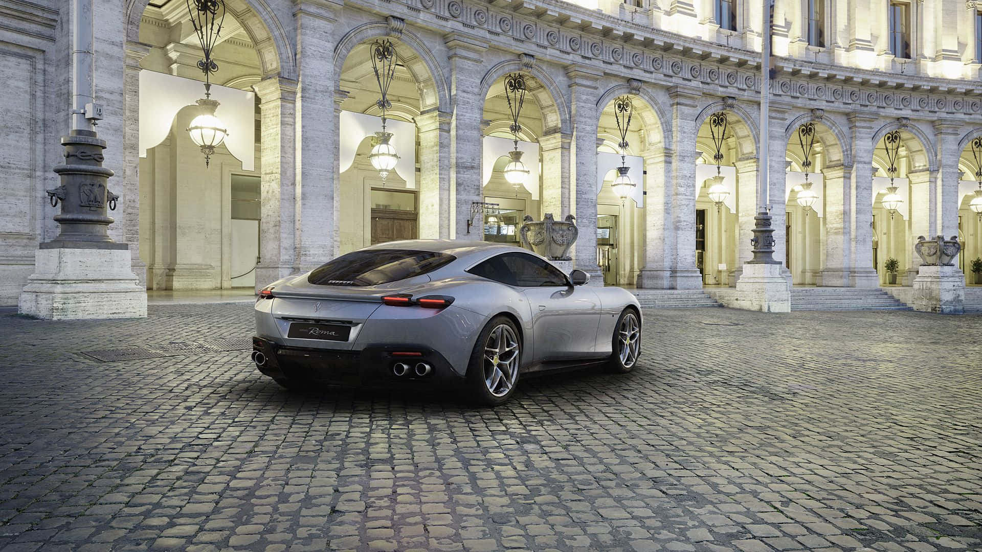 Ferrari Roma 桌布 壁紙 — 一輛時尚的銀色跑車停泊在鵝卵石庭院中，上方是燈火通明的古典建築的巨大拱門。