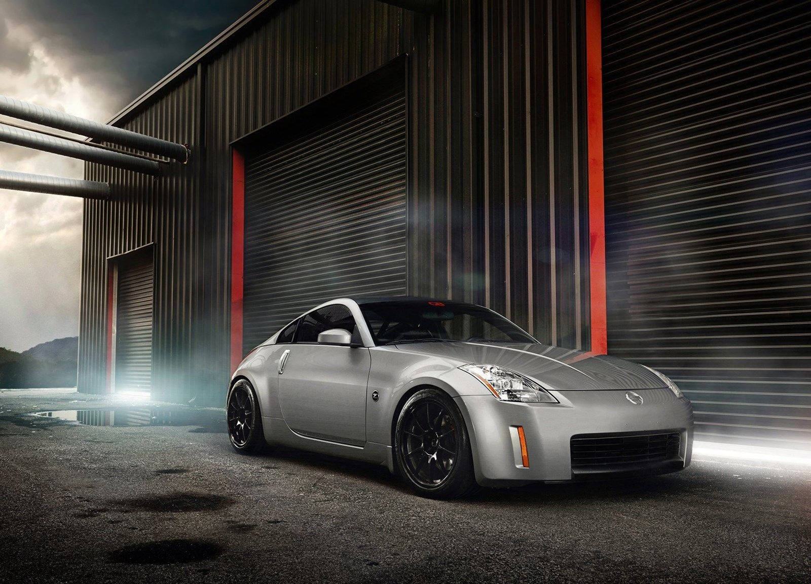 Nissan 350z 桌布 壁紙 — 一輛時尚的銀色跑車在戲劇性燈光下閃耀，位於帶有紅色點綴的波紋金屬倉庫外。