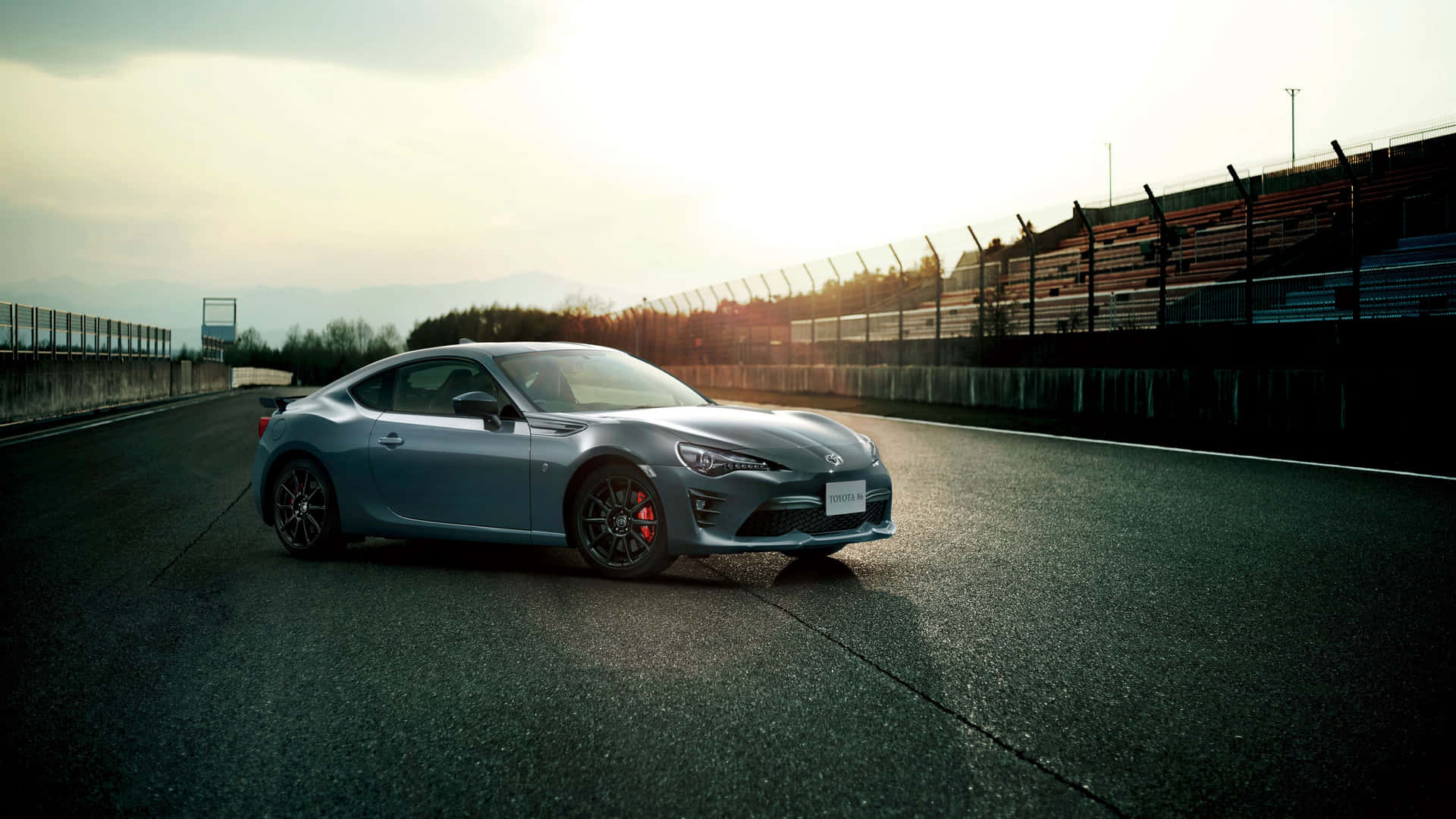 銀色跑車在日落時分的賽道上，背景有山脈。 — Toyota Supra Mk4 壁紙