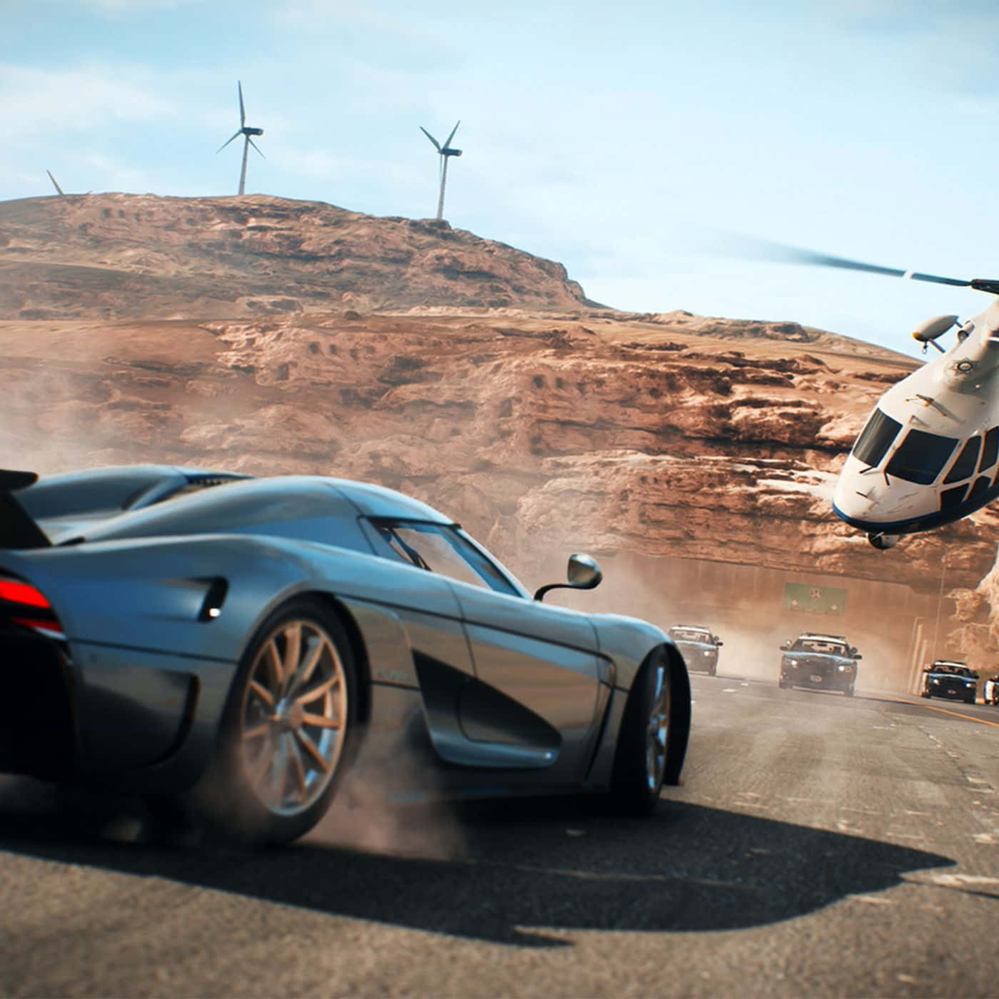 Need For Speed Payback 桌布 壁紙 — 一輛時尚的銀色跑車在沙漠公路上疾馳，附近有直升機盤旋，遠處山丘上有風力發電機。