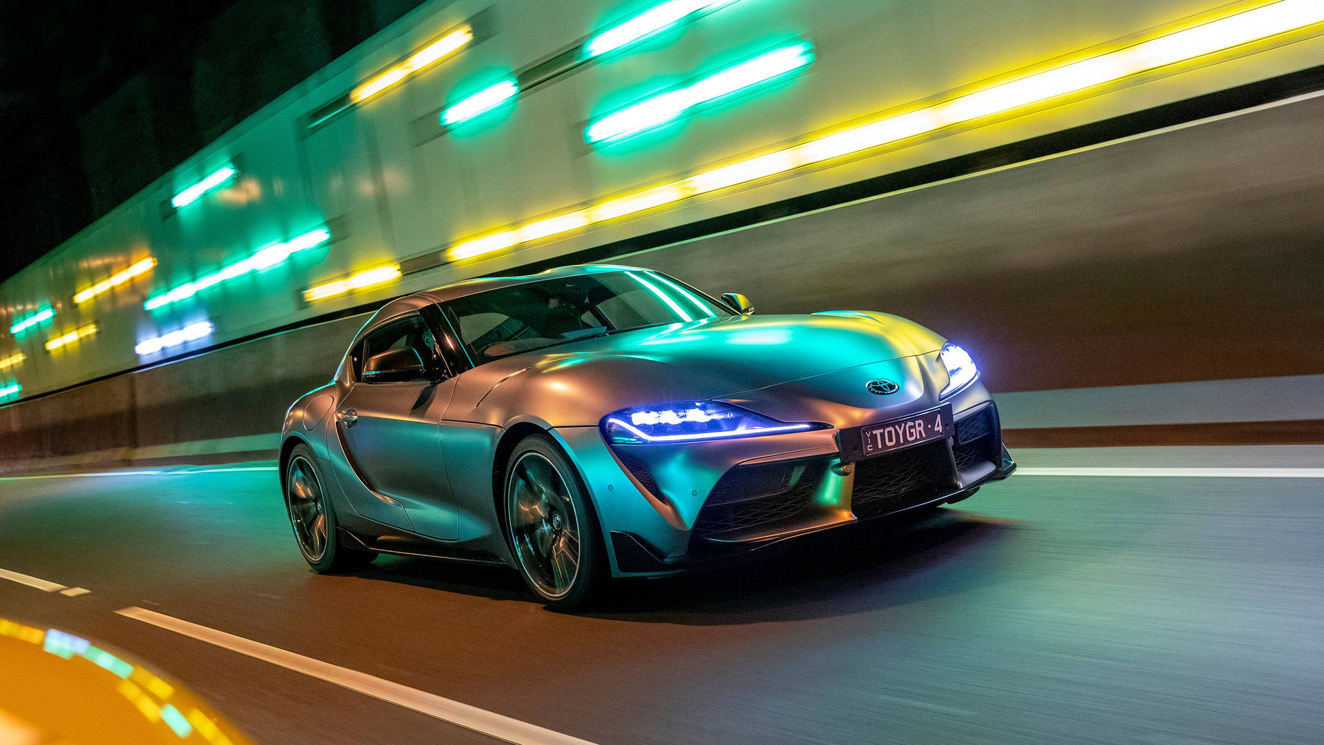 一輛銀色跑車在夜晚的霓虹燈隧道中疾馳。 — Toyota Supra Mk4 壁紙