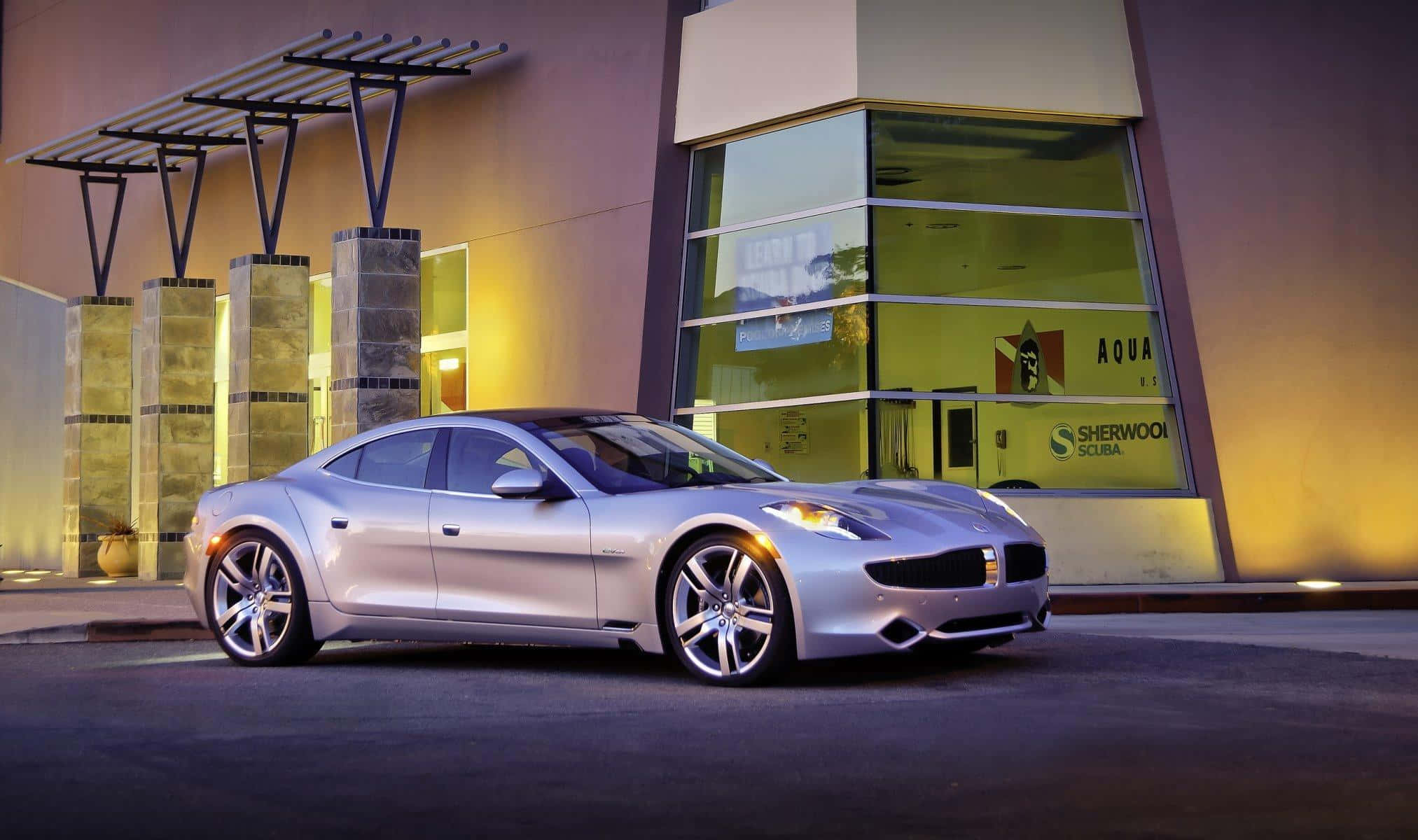 Fisker 桌布 壁紙 — 一輛時尚的銀色跑車在黃昏時停在一棟現代建築前，建築物散發著溫暖的光芒。