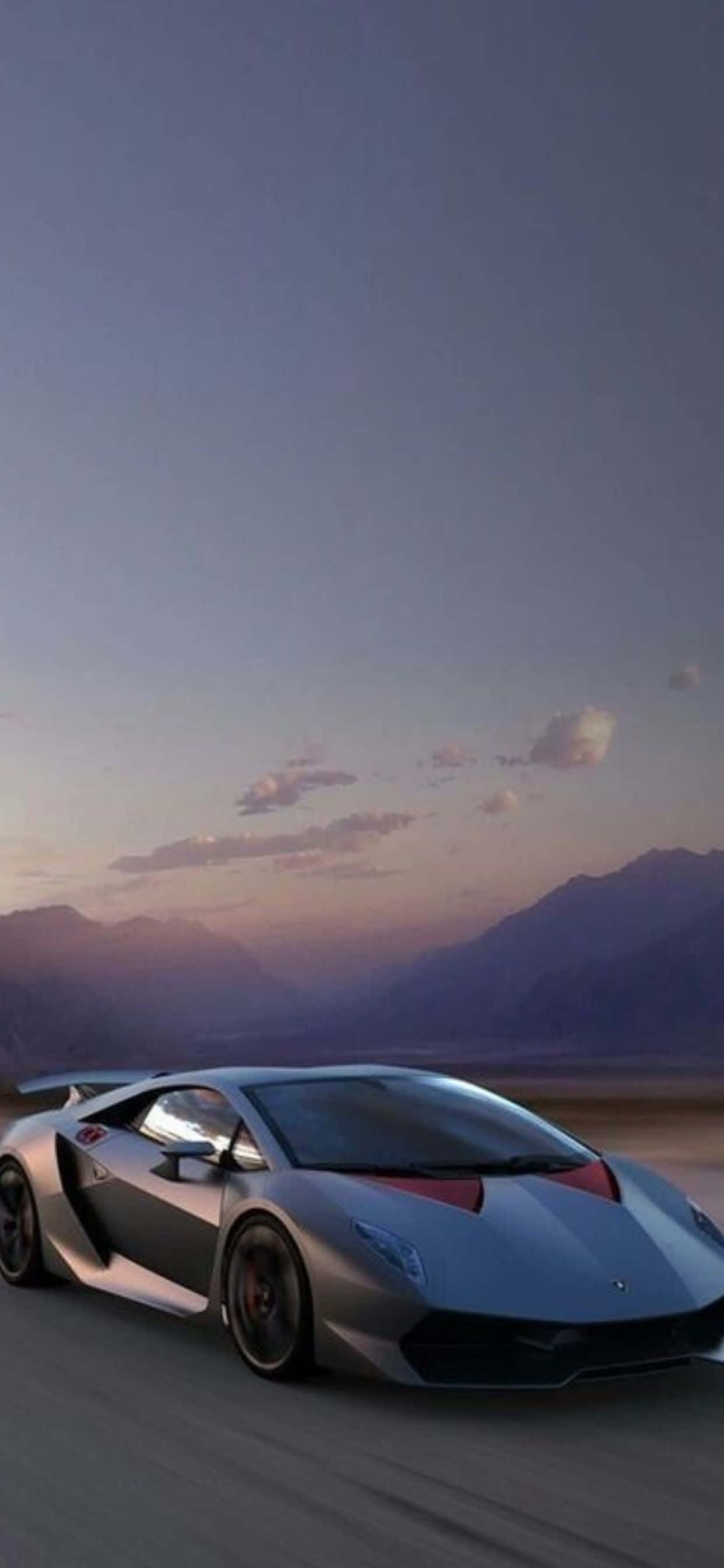 Lamborghini Phone 桌布 壁紙 — 一輛時尚的銀色跑車在黃昏時分疾馳在沙漠公路上，背景是山脈。