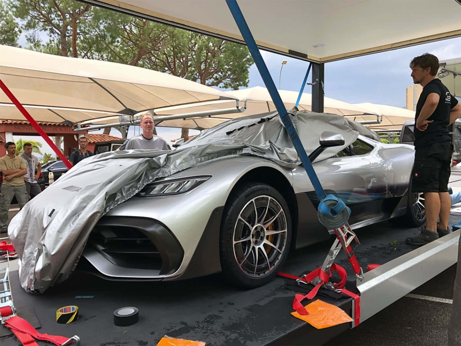Mercedes 桌布 壁紙 — 一輛時尚的銀色跑車部分被灰色防水布覆蓋，並用紅色綁帶固定在運輸平台上。