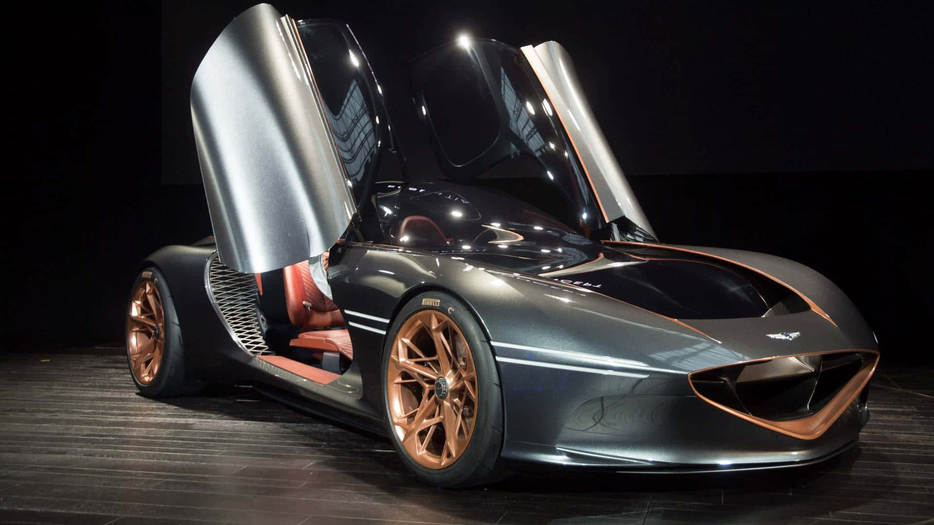 Genesis Essentia 桌布 壁紙 — 一輛時尚的銀色跑車配備鷗翼車門和銅色點綴，在戲劇性的工作室燈光下展示。