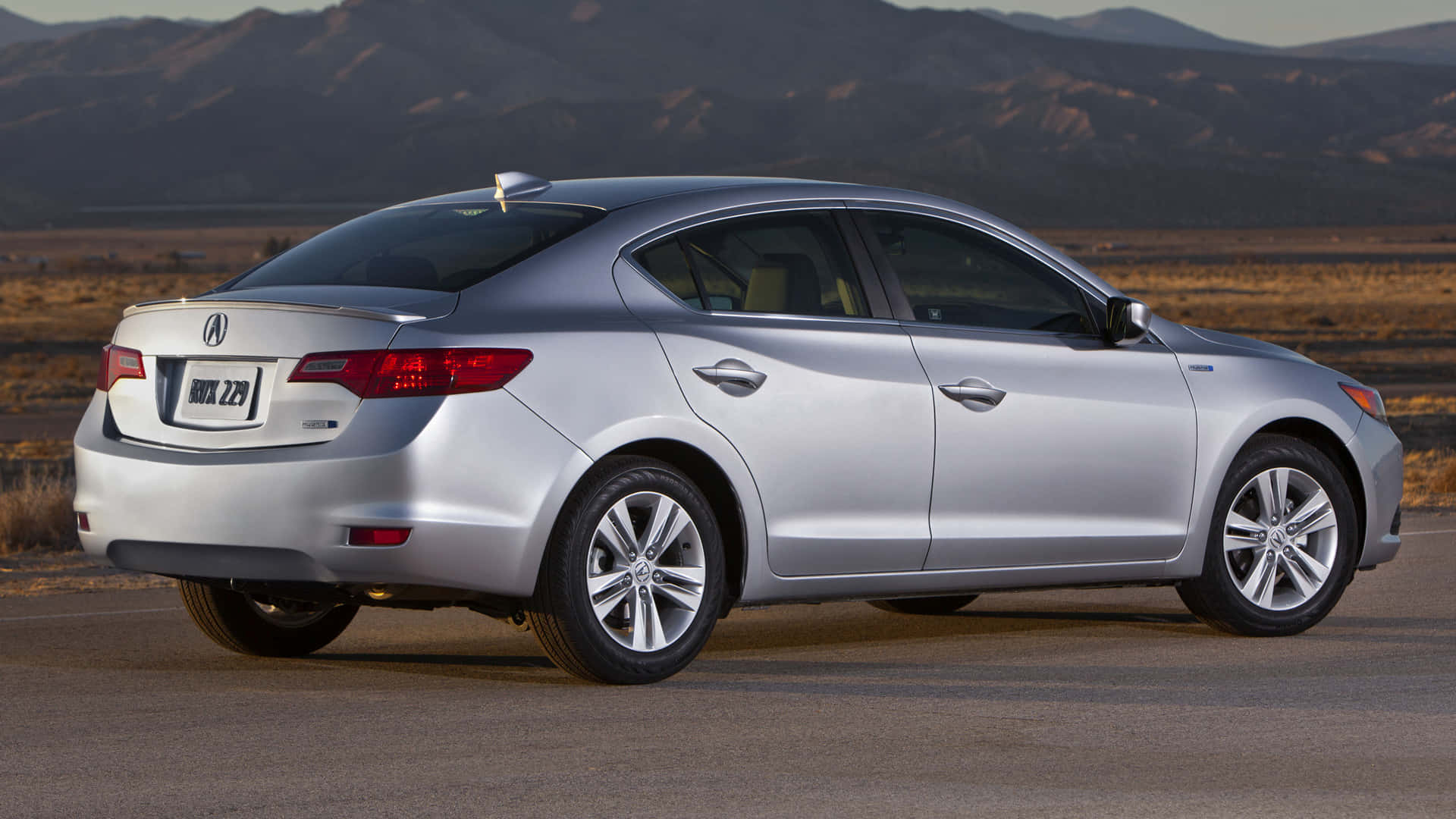 Acura Ilx 桌布 壁紙 — 一輛時尚的銀色轎車停在沙漠公路上，背景是山脈，正值黃金時刻。