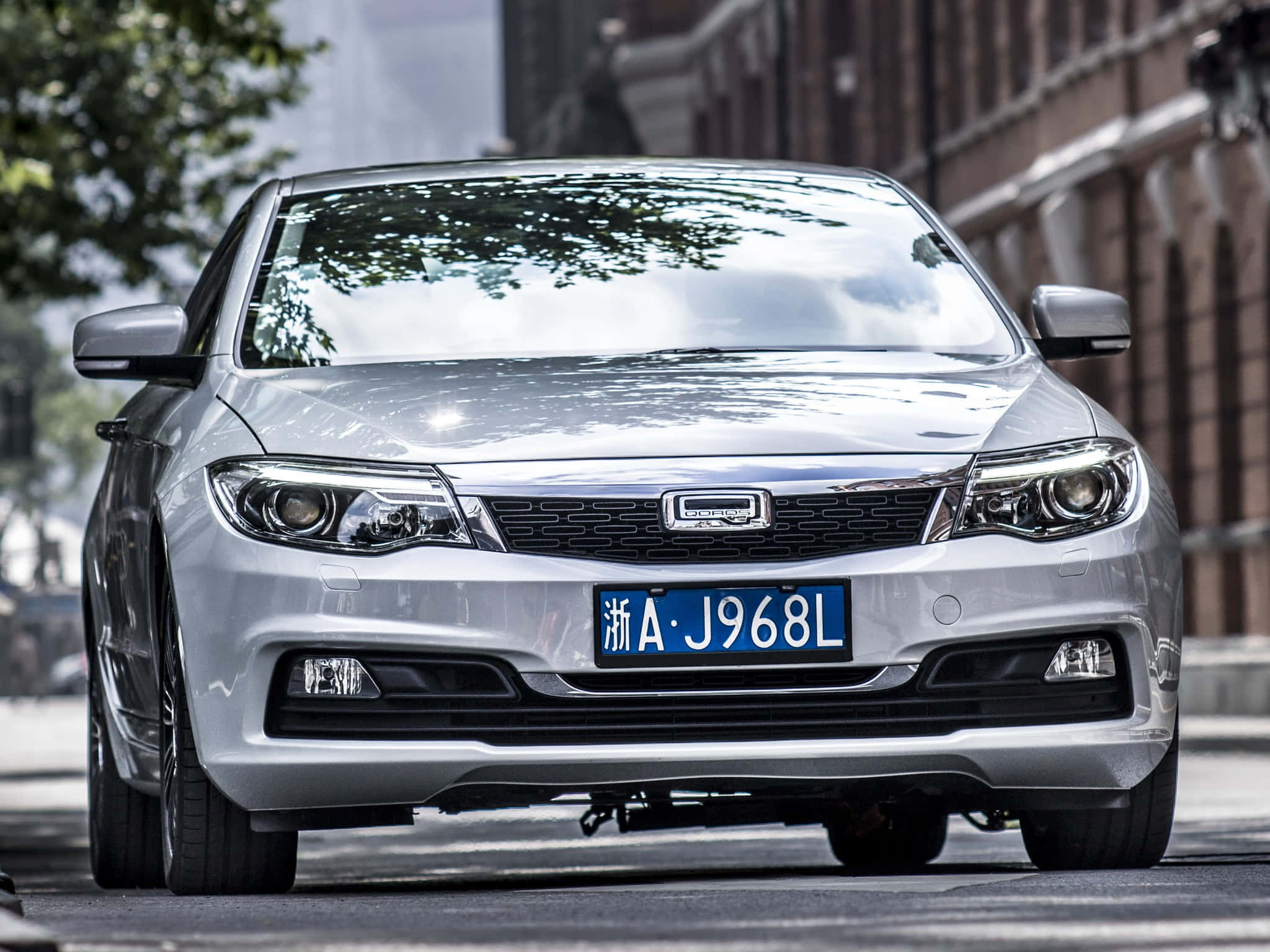 Qoros 桌布 壁紙 — 一輛時尚的銀色轎車停放在城市的街道上，背景有樹木和磚砌建築。