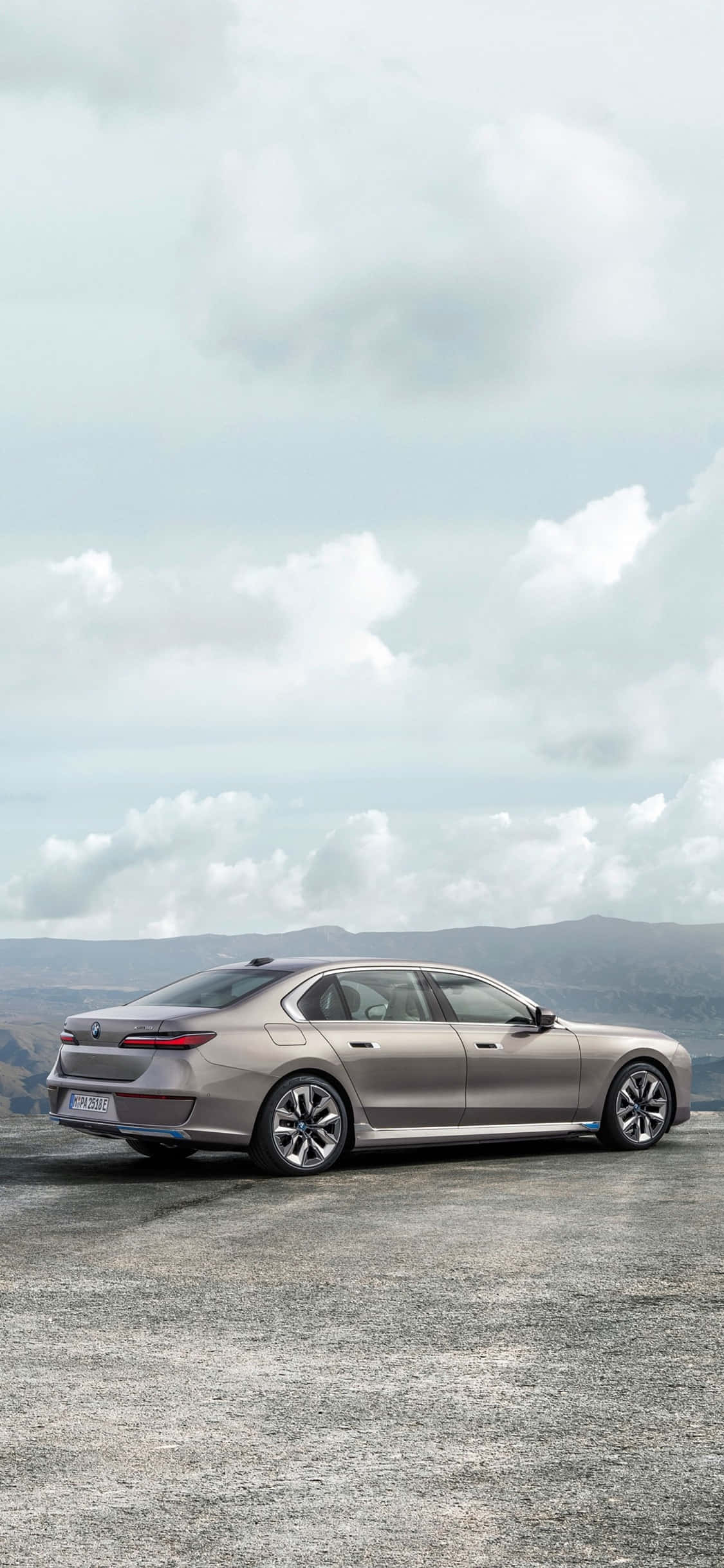 iPhone X Bmw 桌布 壁紙 — 一輛時尚的銀色轎車停泊在碎石觀景點，遠山在陰天之下。