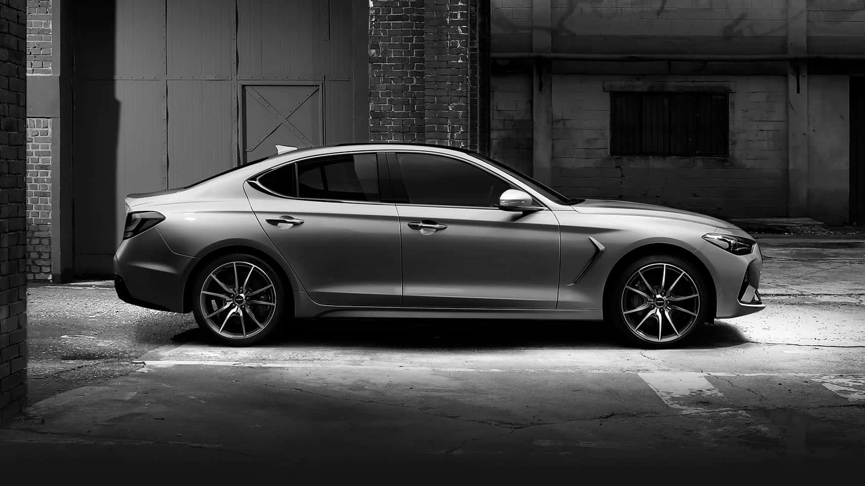 Genesis G70 桌布 壁紙 — 一輛時尚的銀色轎車停泊在粗糙的城市小巷中，周圍是磚牆和工業質感，在戲劇性的單色燈光下。
