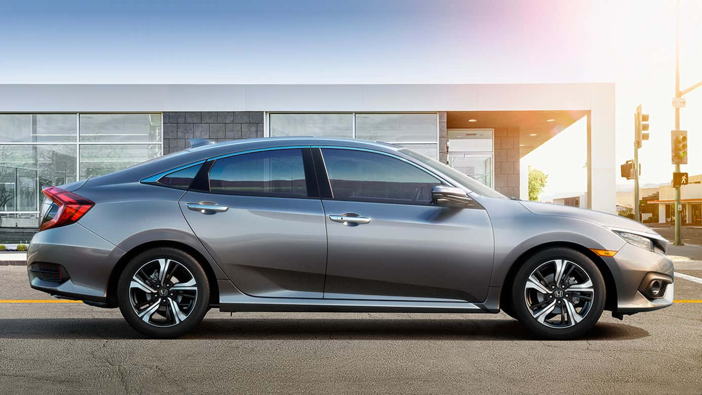 Hatchback 桌布 壁紙 — 一輛時尚的銀色轎車停泊在陽光明媚的街道上，旁邊是一座帶玻璃窗的現代建築。