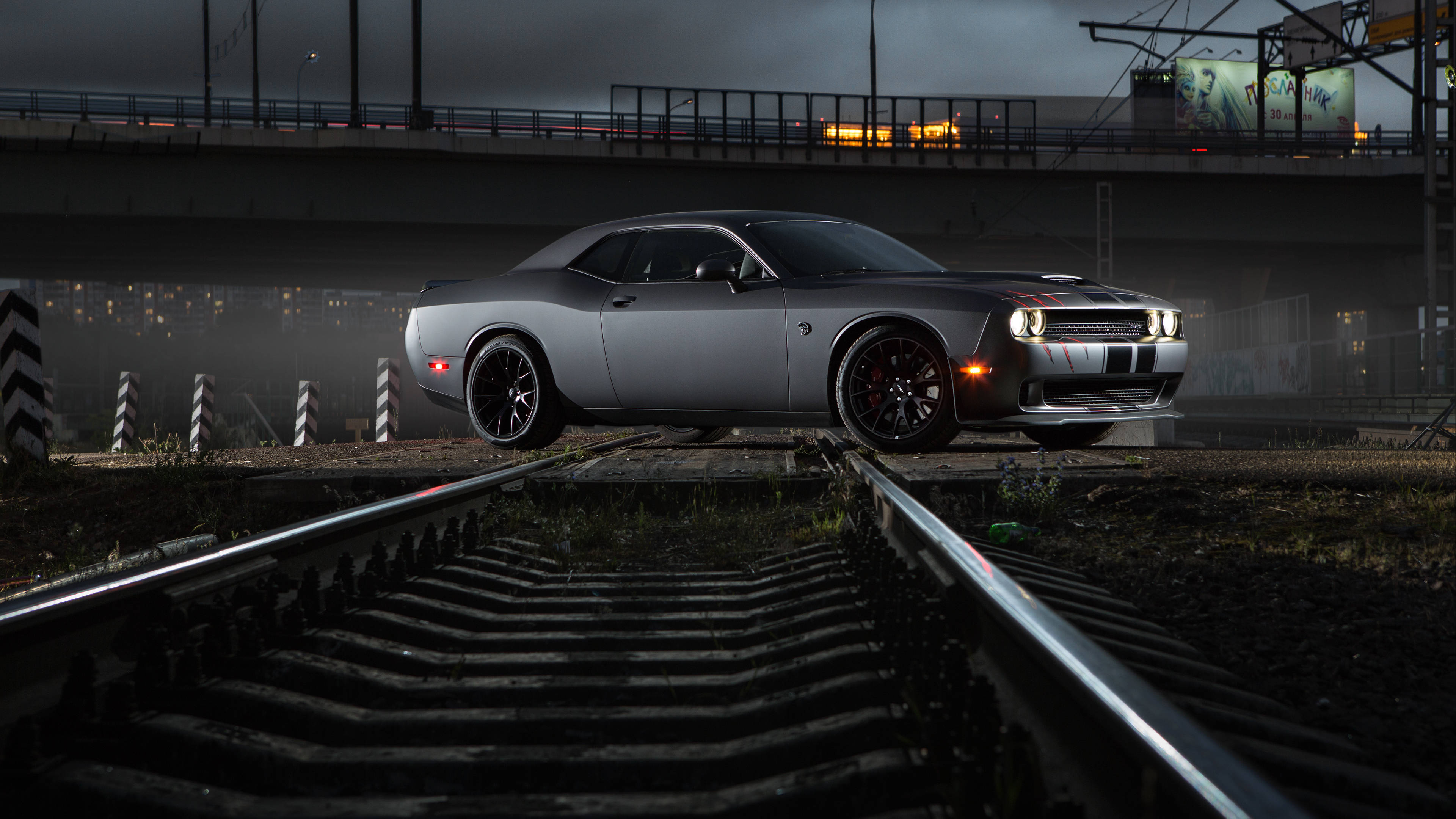 Dodge 桌布 壁紙 — 一輛時尚的銀色道奇挑戰者停在磨損的火車軌道上，位於黑暗的城市天橋下，車頭燈閃爍。