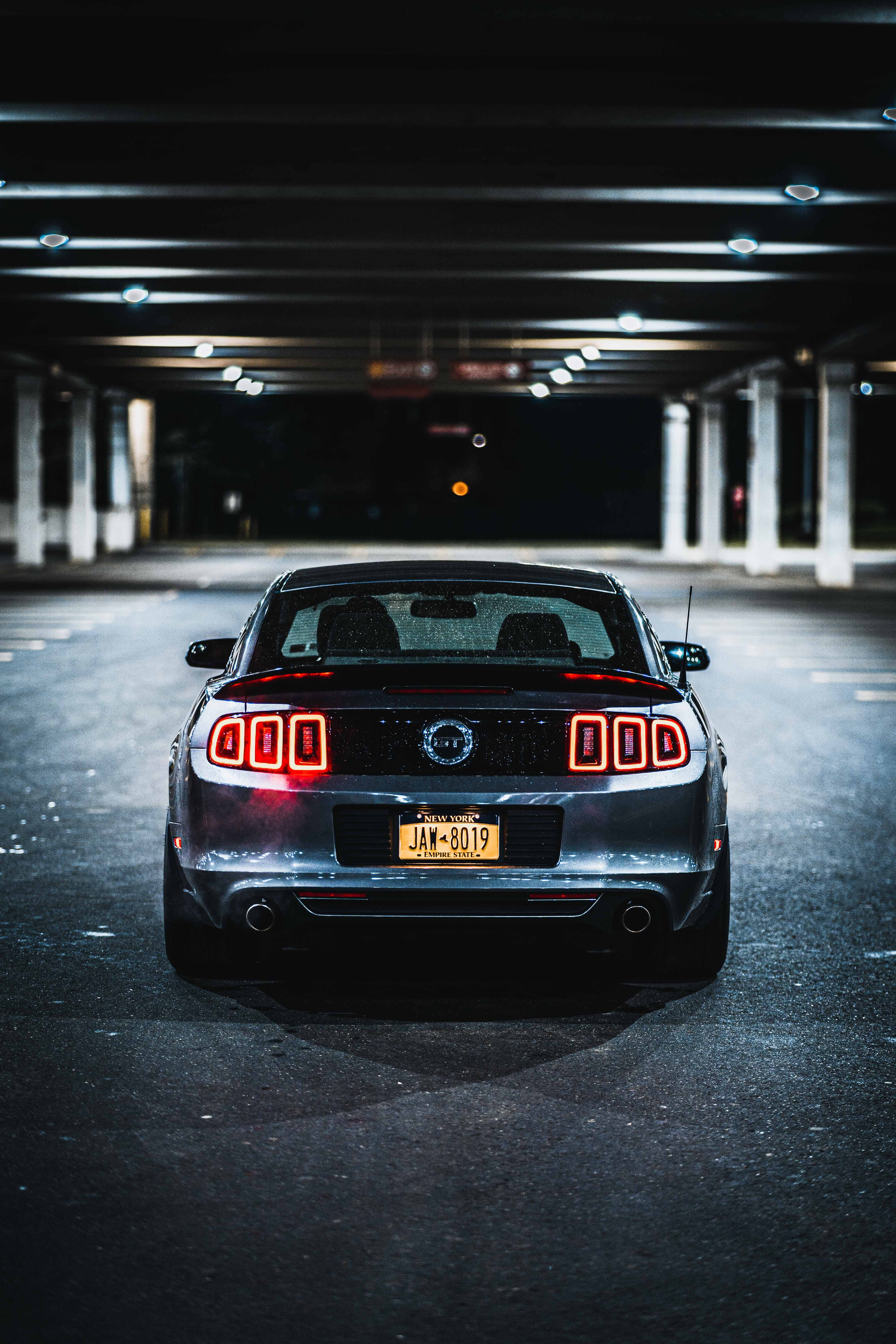 Cool Mustang 桌布 壁紙 — 一輛時尚的銀色野馬跑車，紅色尾燈發光，夜晚停泊在昏暗的城市天橋下。